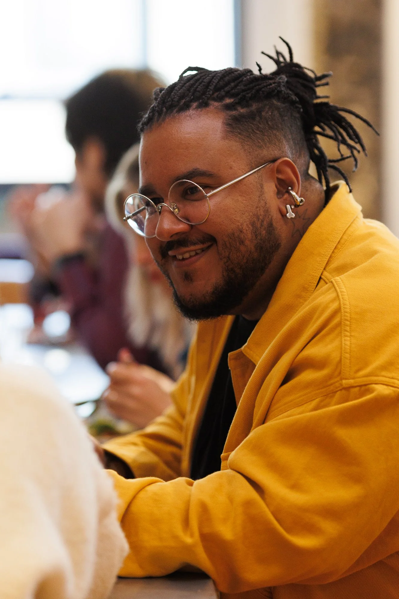 A smiling man with glasses and a yellow jacket engaging in conversation at a creative industry meetup.