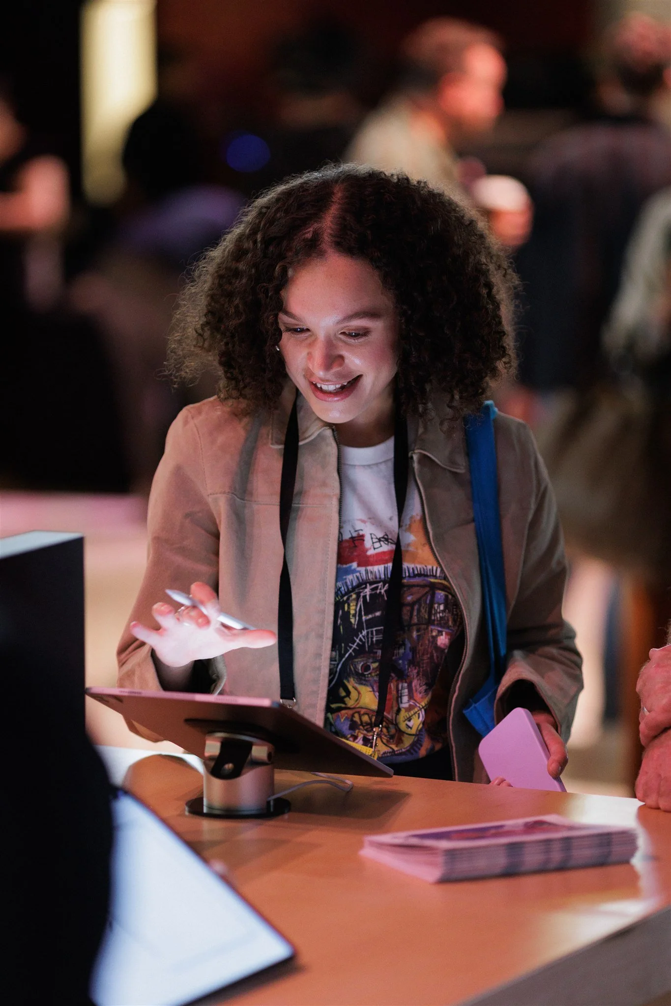 A smiling woman with curly hair using a stylus on a tablet at a creative festival exhibition.