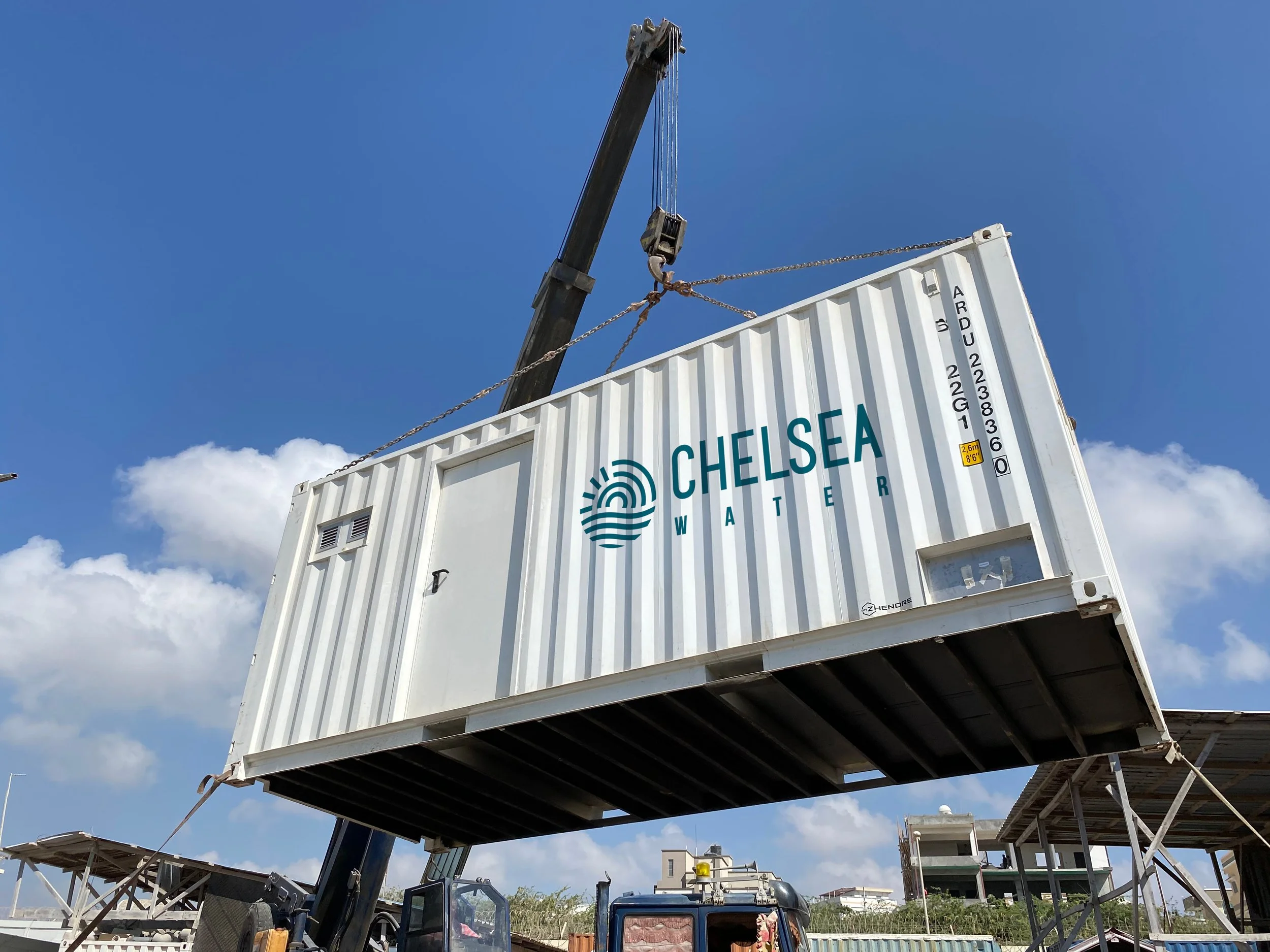 A modular water treatment in a container featuring the Chelsea Water logo being lowered into position by a crane.