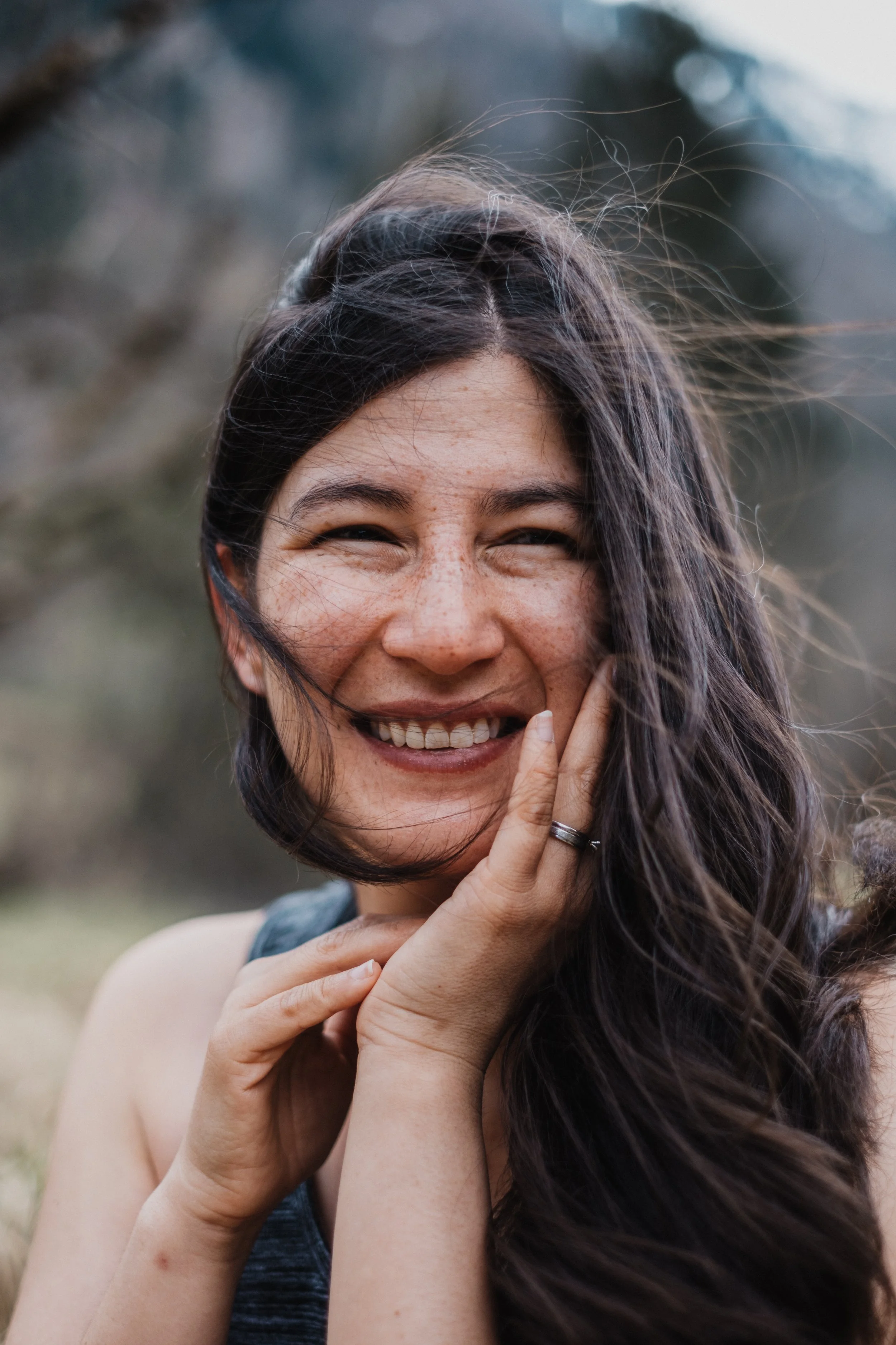 Lächelnder Frau mit langen dunklen Haaren im Freien, bei Wind.