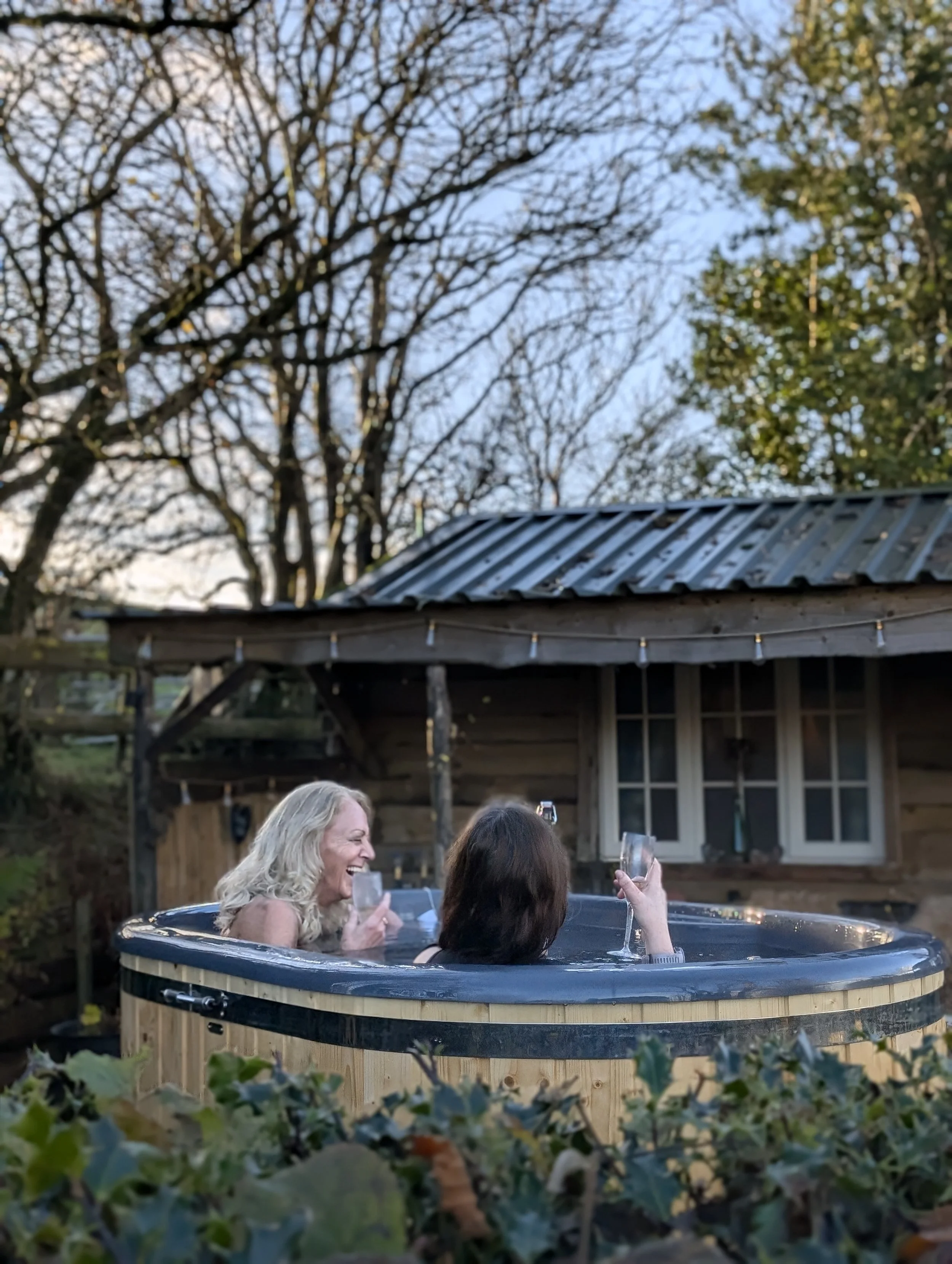 A steaming wood-fired hot tub outside a cosy cabin in Mid Wales, overlooking rolling countryside, perfect for a girls’ weekend away filled with long chats and laughter.