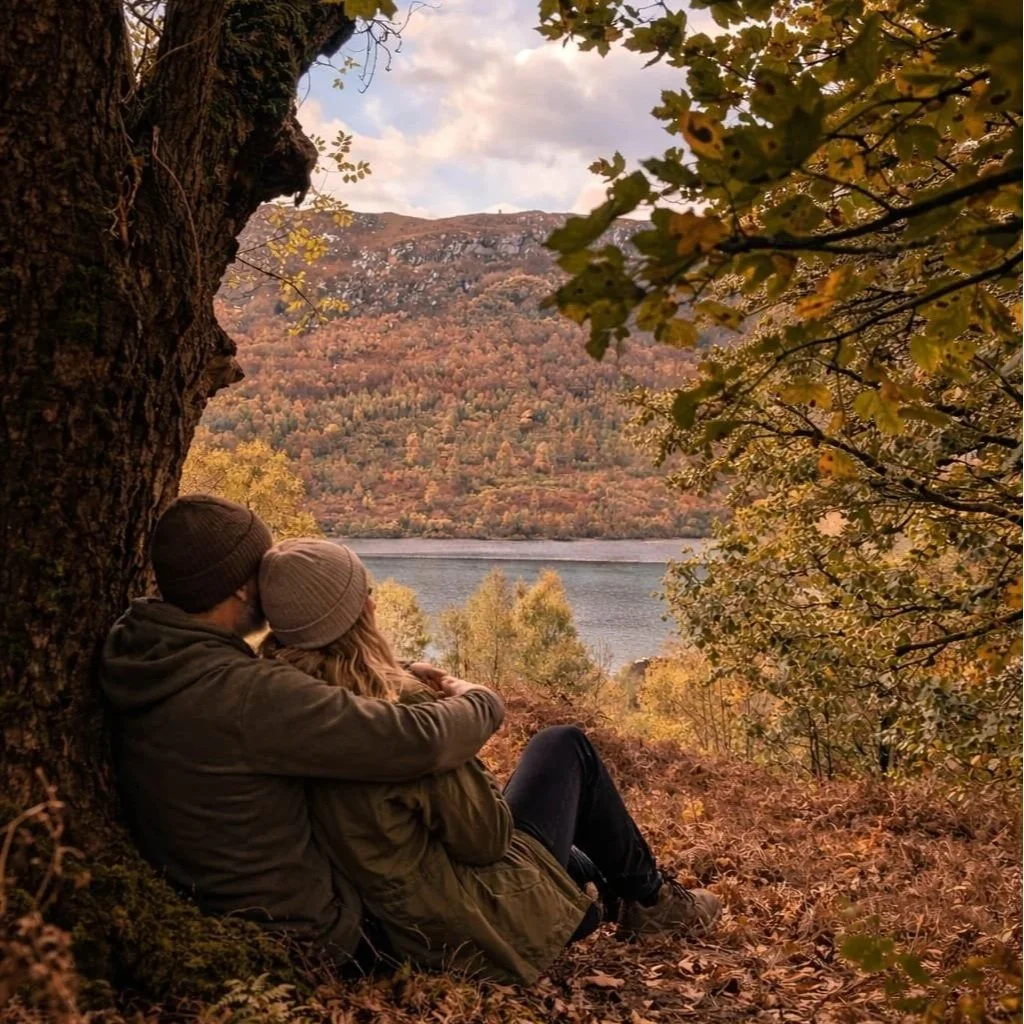 Couple relaxing against a tree overlooking a lake in the Elan Valley, enjoying a peaceful forest bathing moment in Mid Wales.