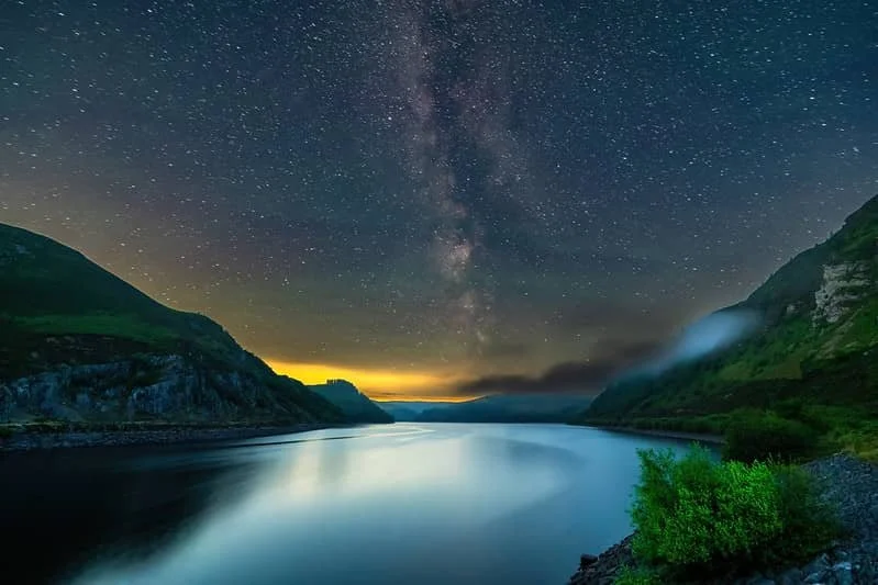 Wide view of the Elan Valley landscape under a dark sky in Wales, with rolling hills silhouetted beneath a clear night sky