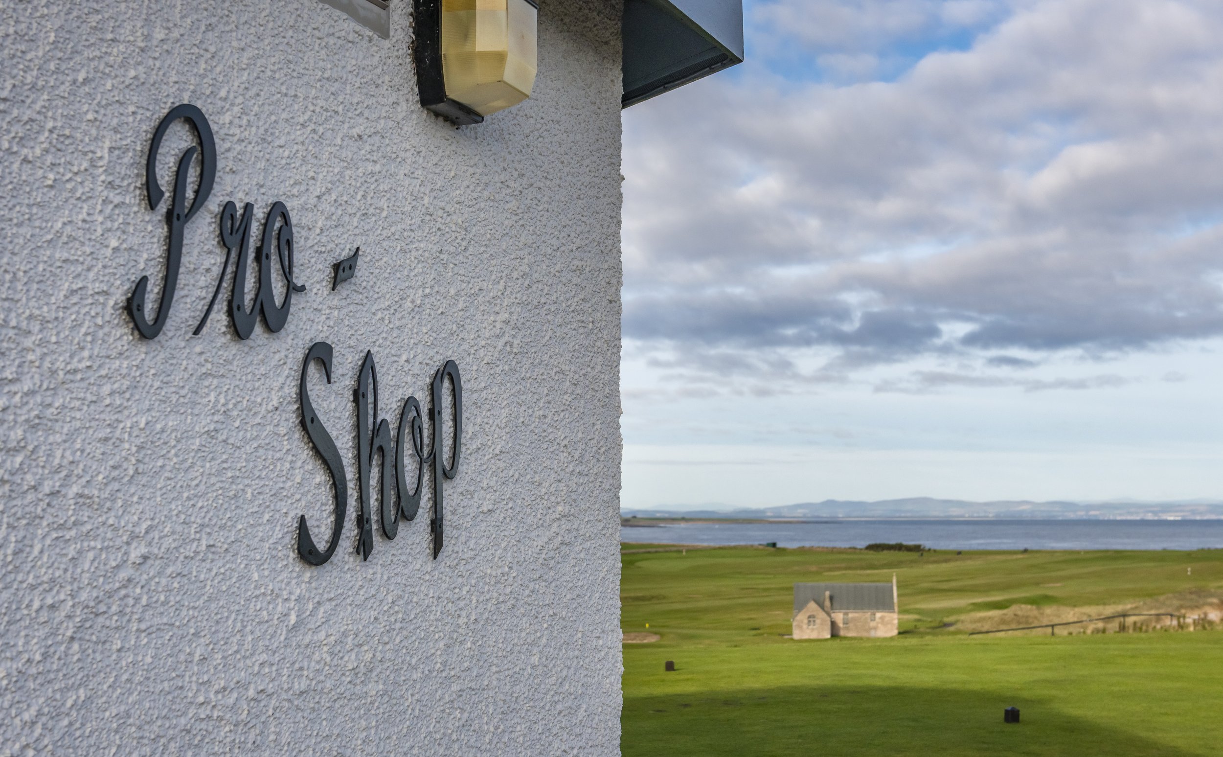 Pro Shop sign on building near golf course with ocean and hills in the background