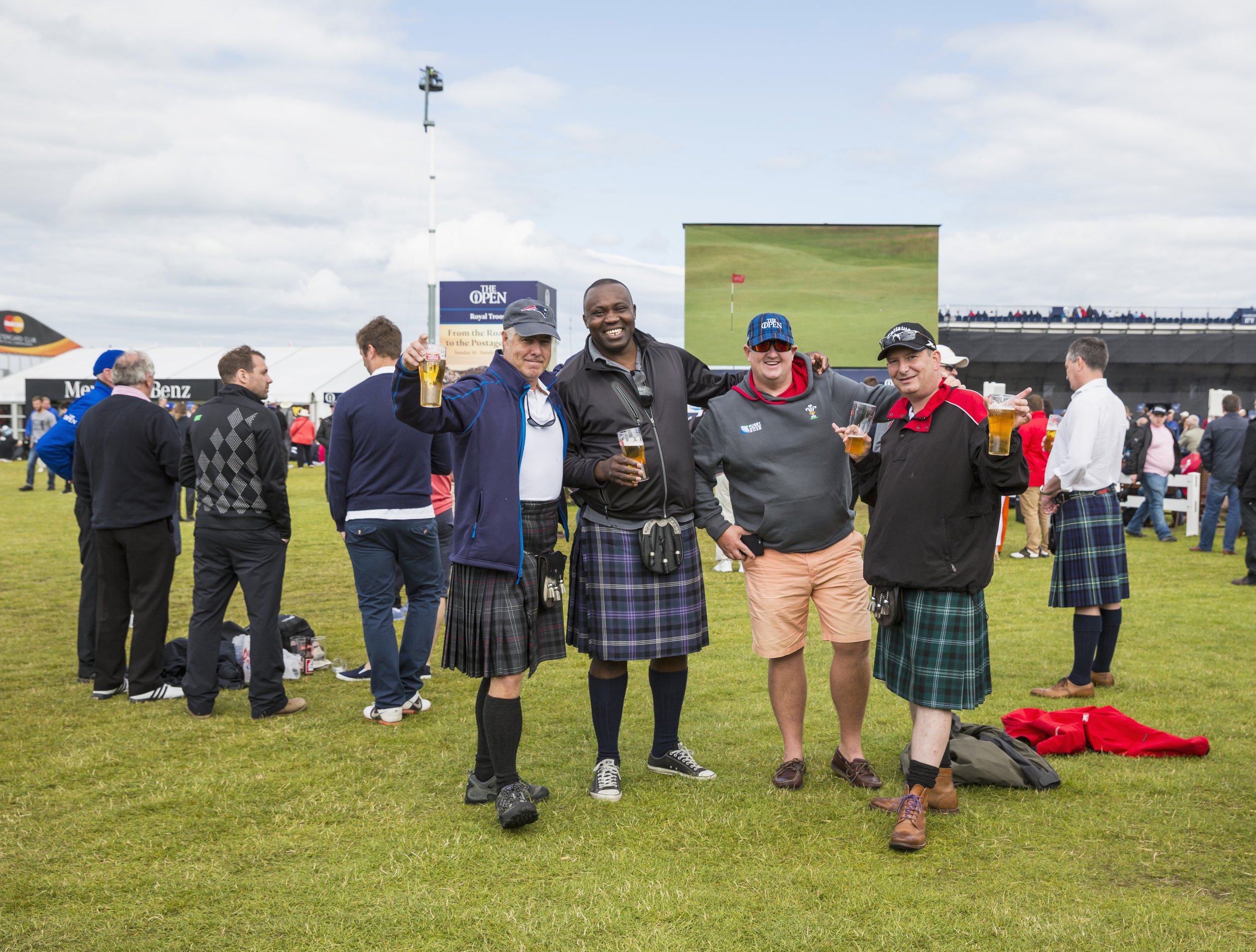 Group of men in kilts holding beers at a golf event.
