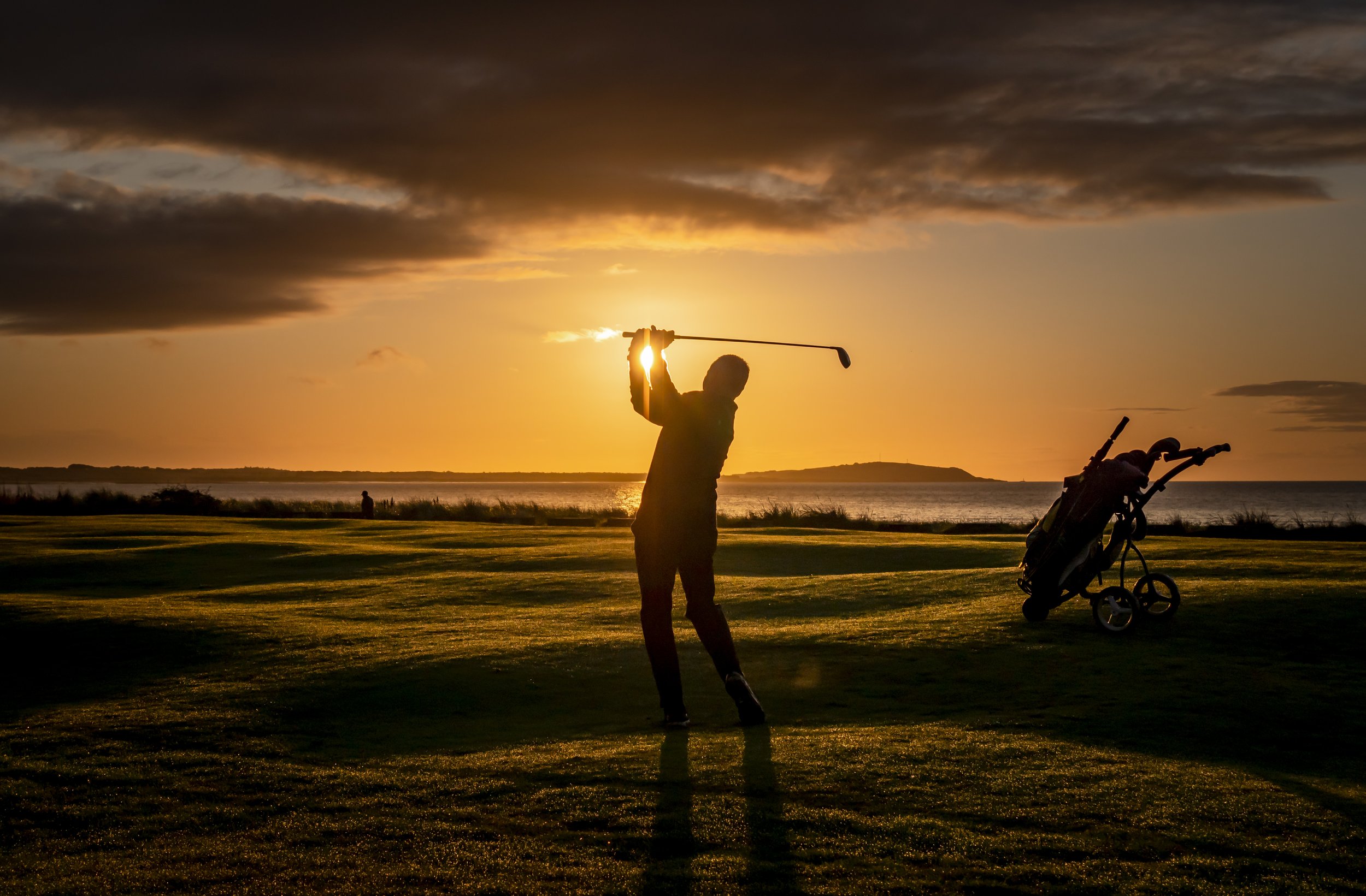 Silhouette of a golfer swinging a club on a golf course at sunset.