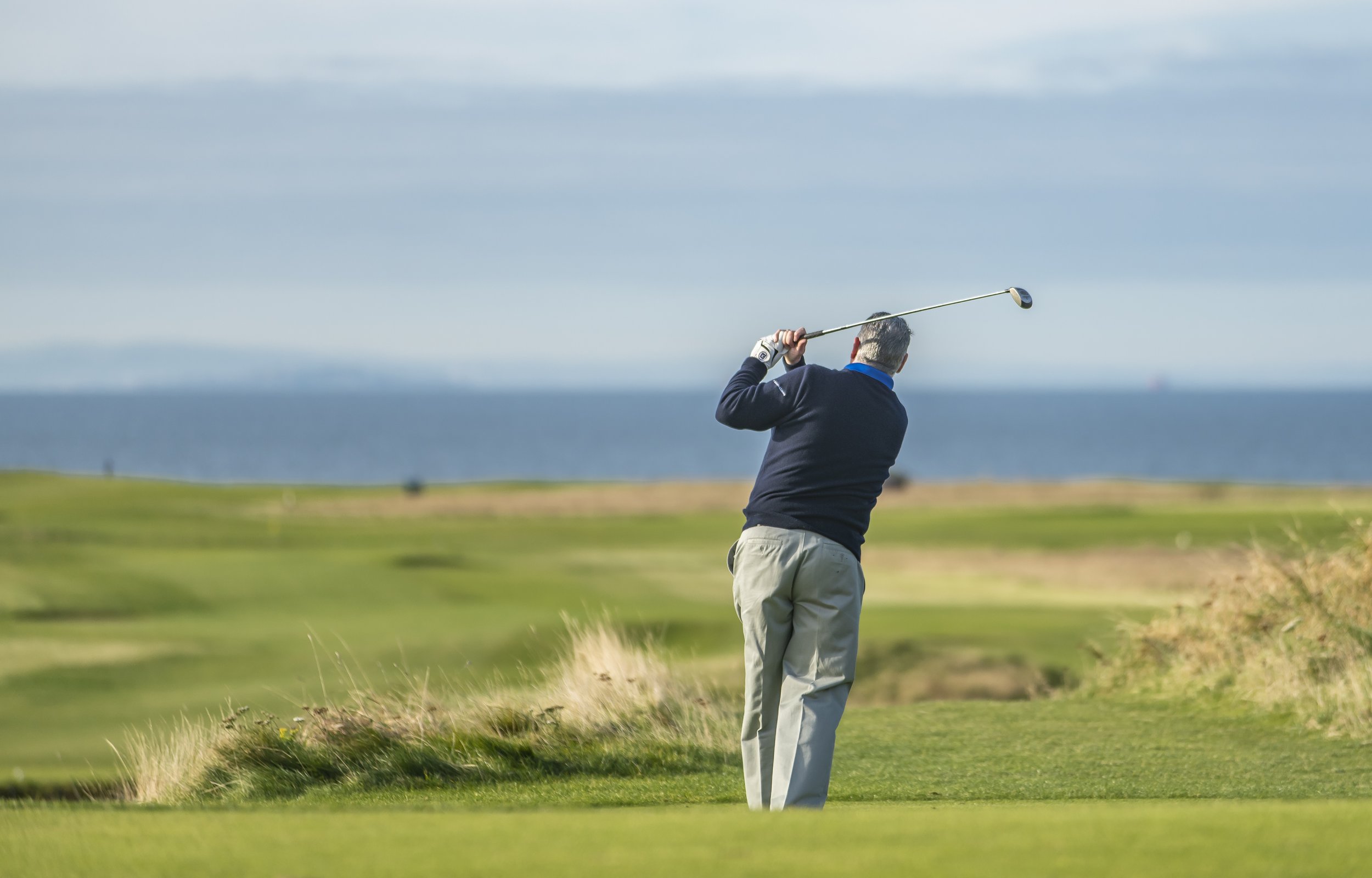 Golfer swinging on a coastal golf course with ocean backdrop