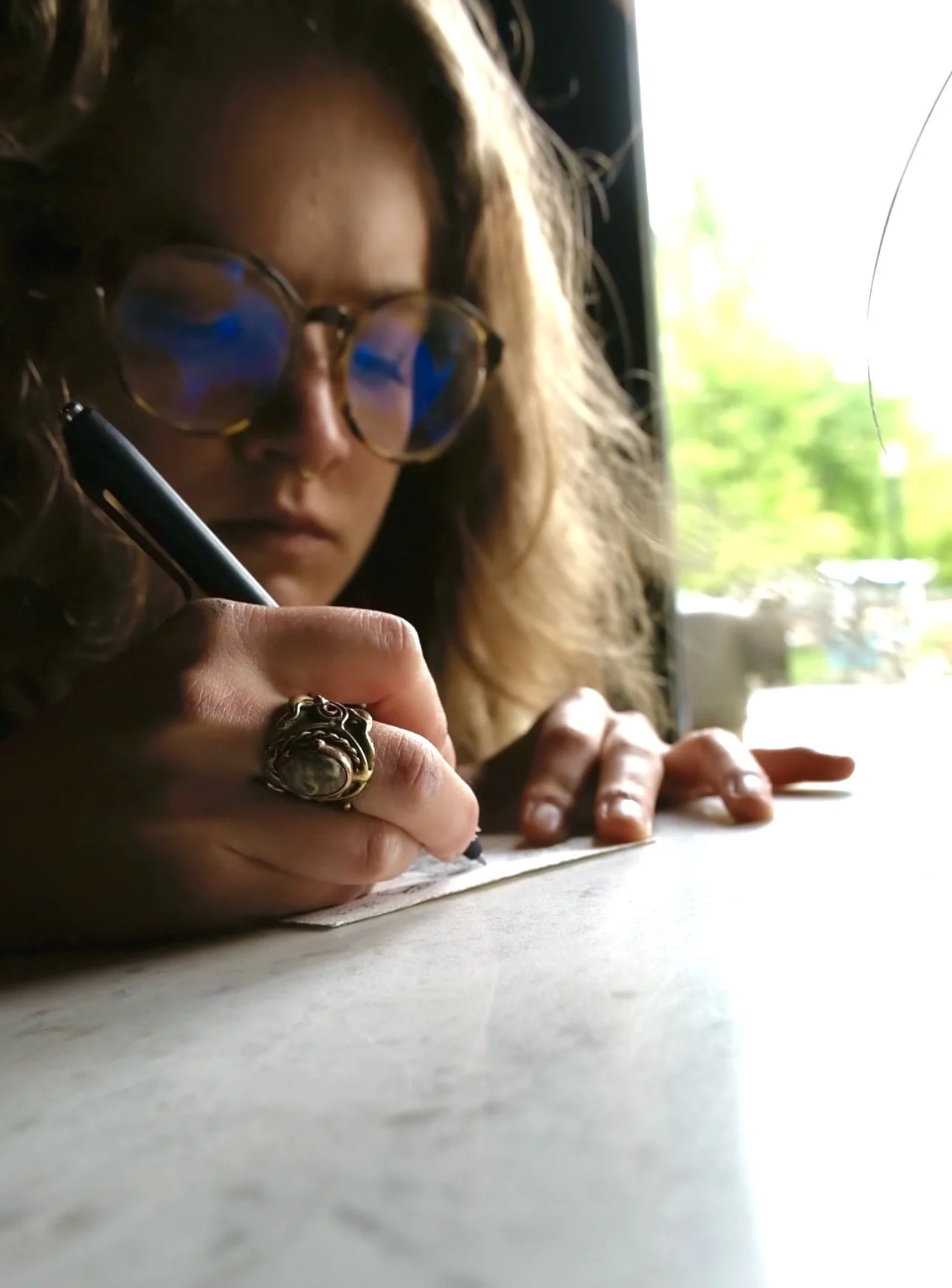 Girl with glasses looking down at a picture she is drawing. She is wearing a large ornate ring