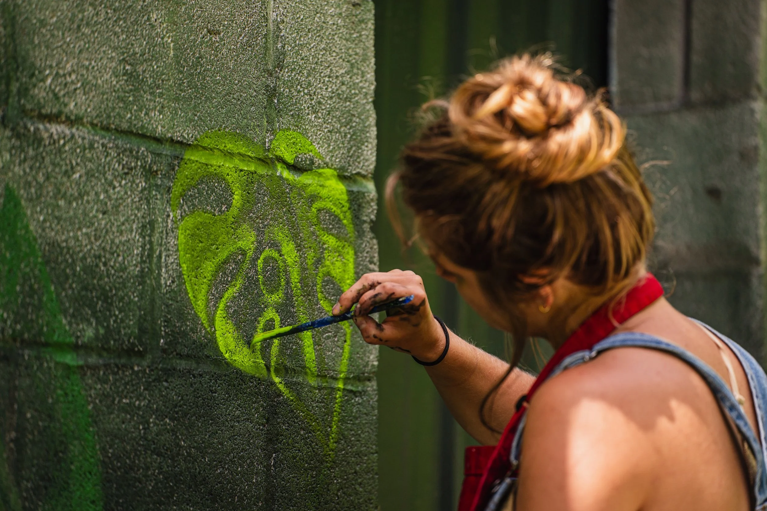Artist painting a monstera leaf design on a concrete wall