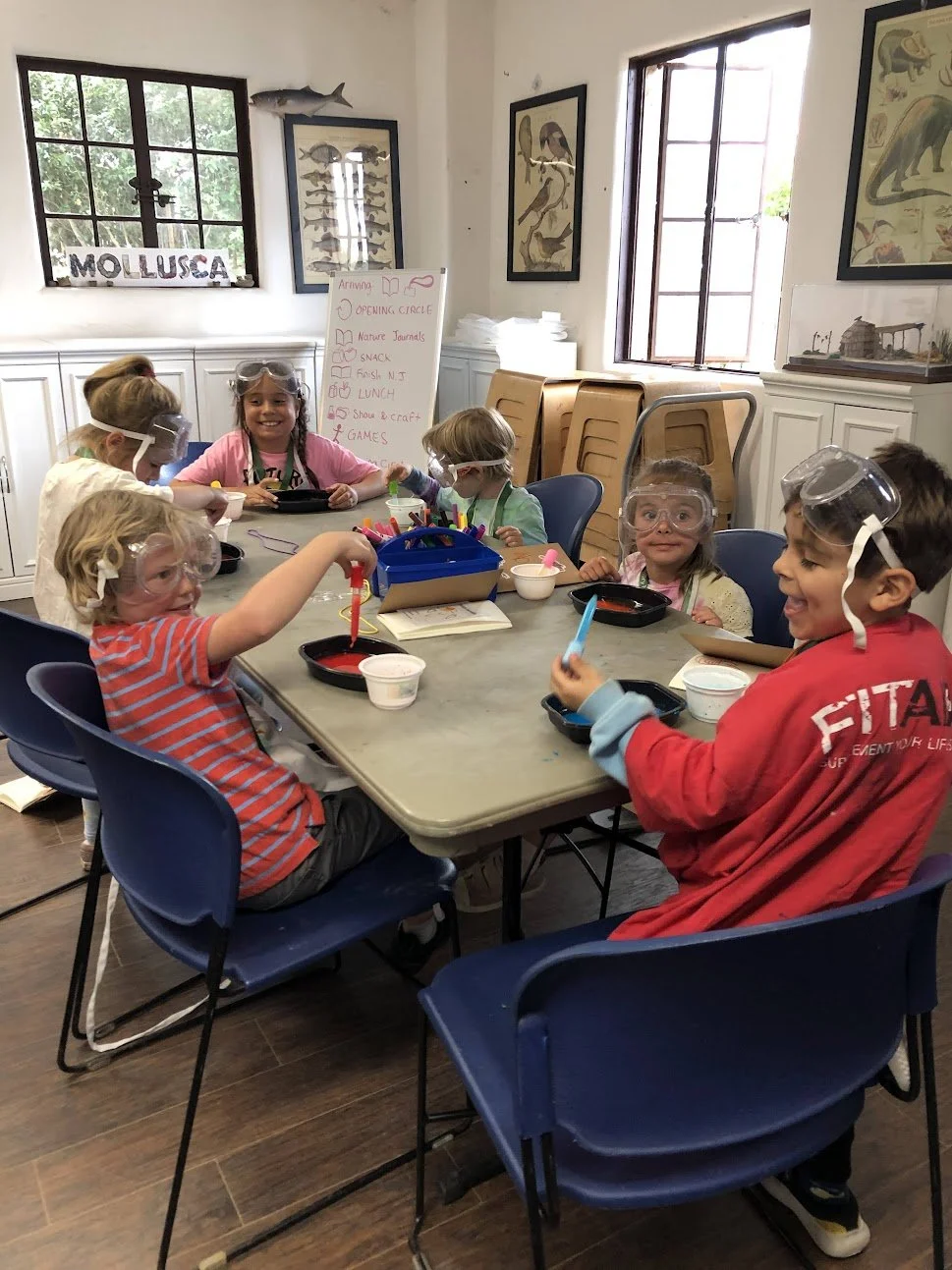 Children in safety goggles smiling as they play with colorful liquid.