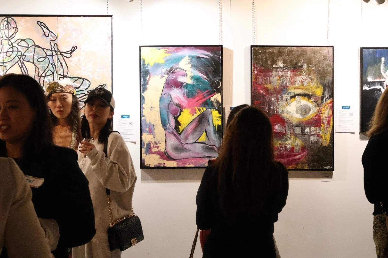 Visitors at an art gallery viewing abstract and figurative paintings.