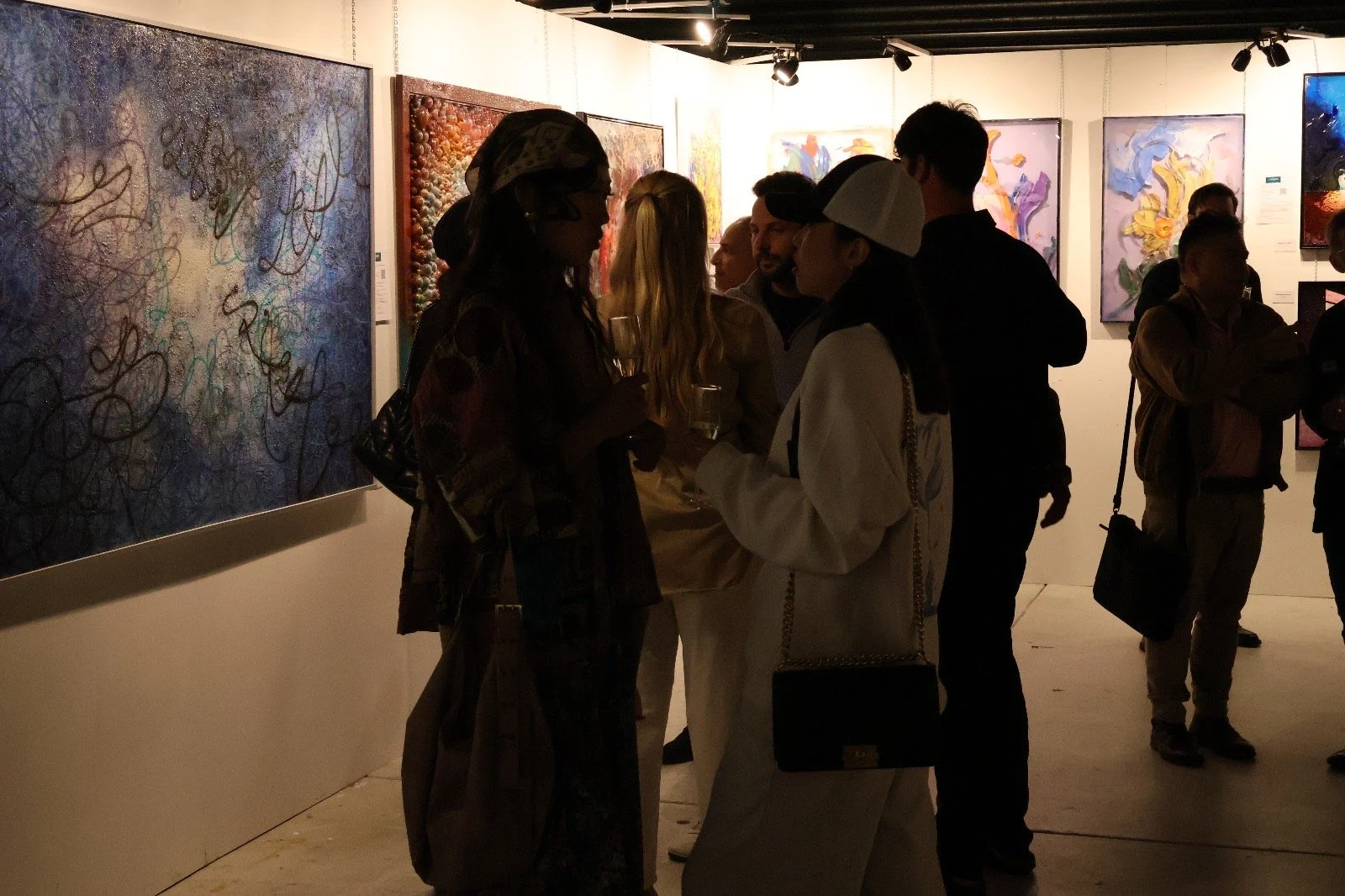 People in an art gallery observing and discussing abstract paintings on the walls.