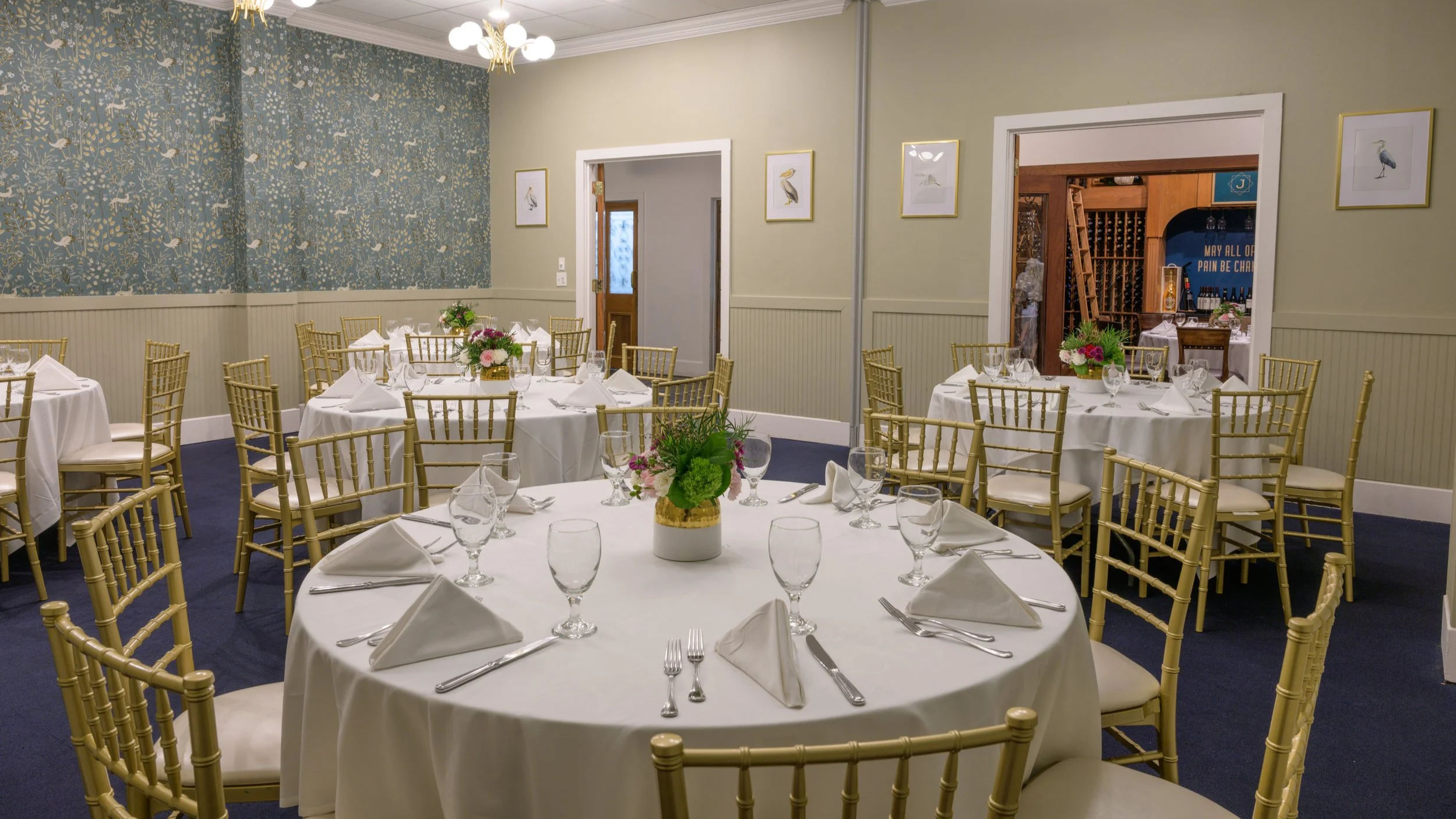 Conference room with long table and chairs, set for a formal meeting or banquet, featuring white tablecloths, glassware, and floral centerpieces, with two televisions on the walls.