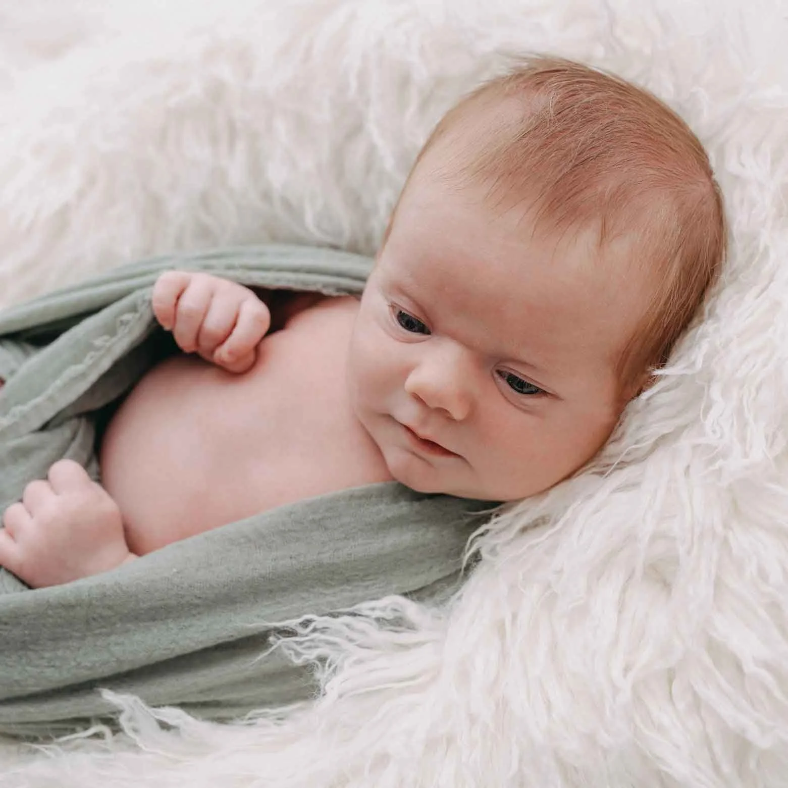 Ein neugeborenes Baby liegt auf einem weissen Kissen eingewickelt in einen grünes Tuch.