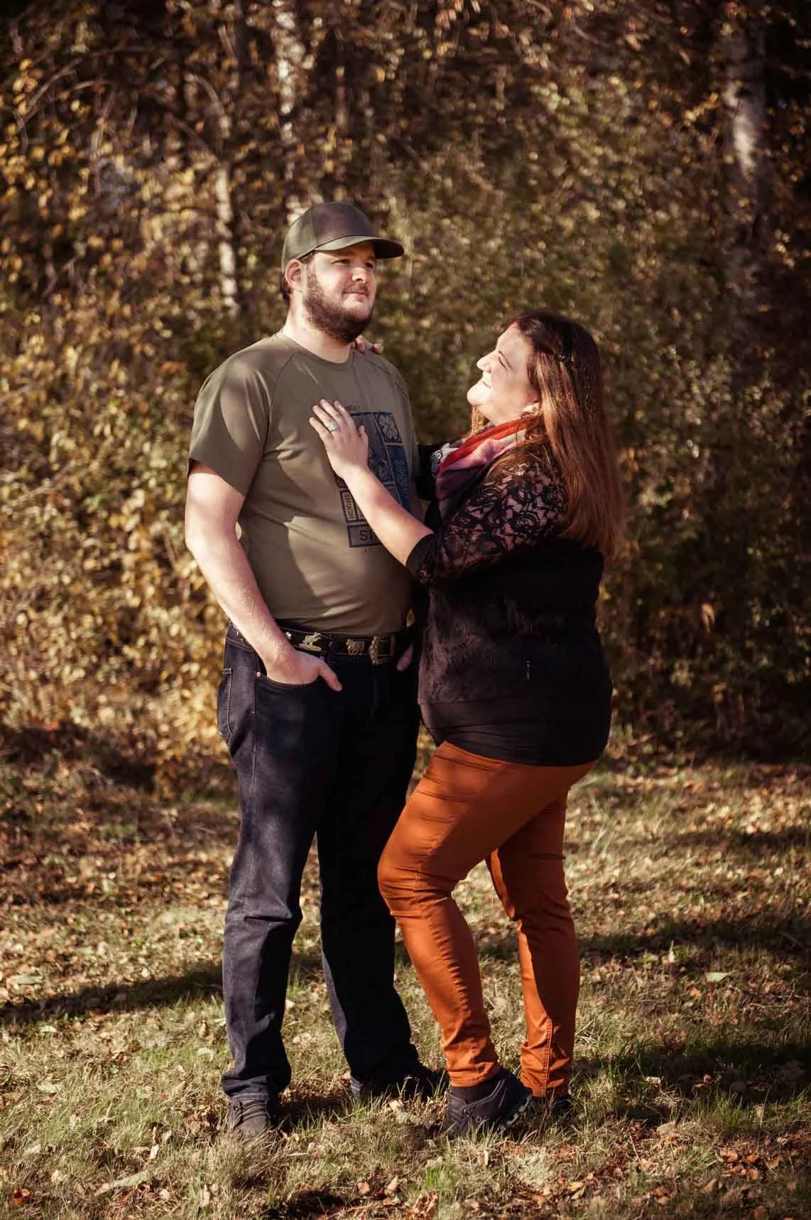 Ein Mann und eine Frau stehen sich in einem Wald gegenüber, die Frau fasst den Mann am Oberkörper und schaut ihn lachend an.