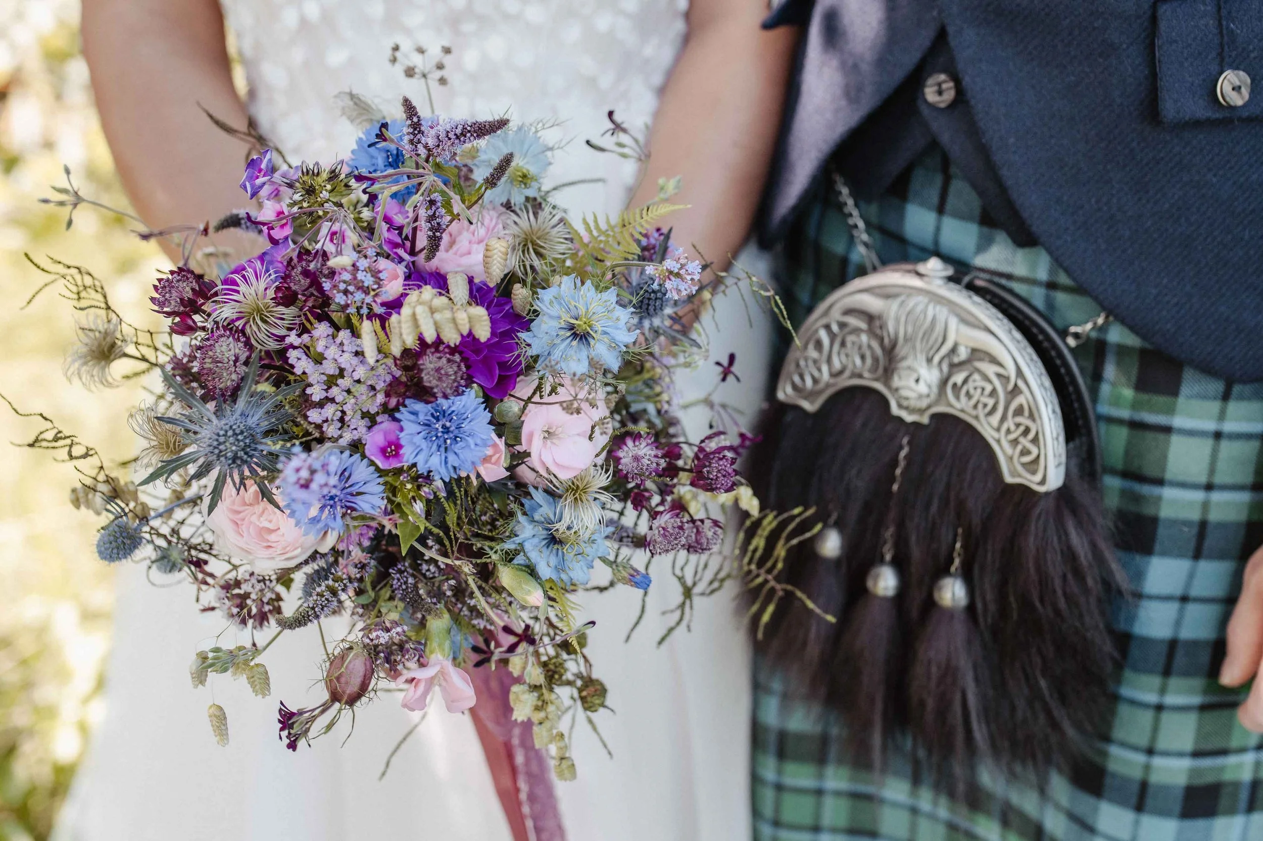 Brautpaar bei einer Hochzeit, die Braut hält einen bunten Brautstrauss, der Bräutigam trägt keltischen Schildanhänger und Schotten-Kragen.