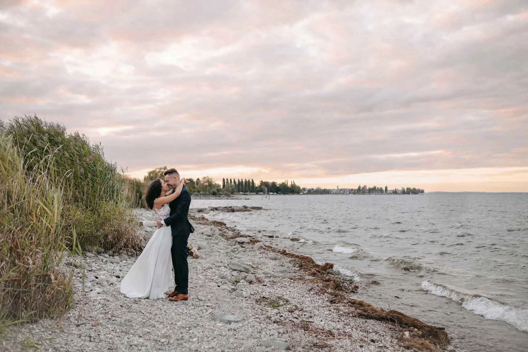 Brautpaar am Seeufer schauen sich tief in die Augen und umarmen sich.
