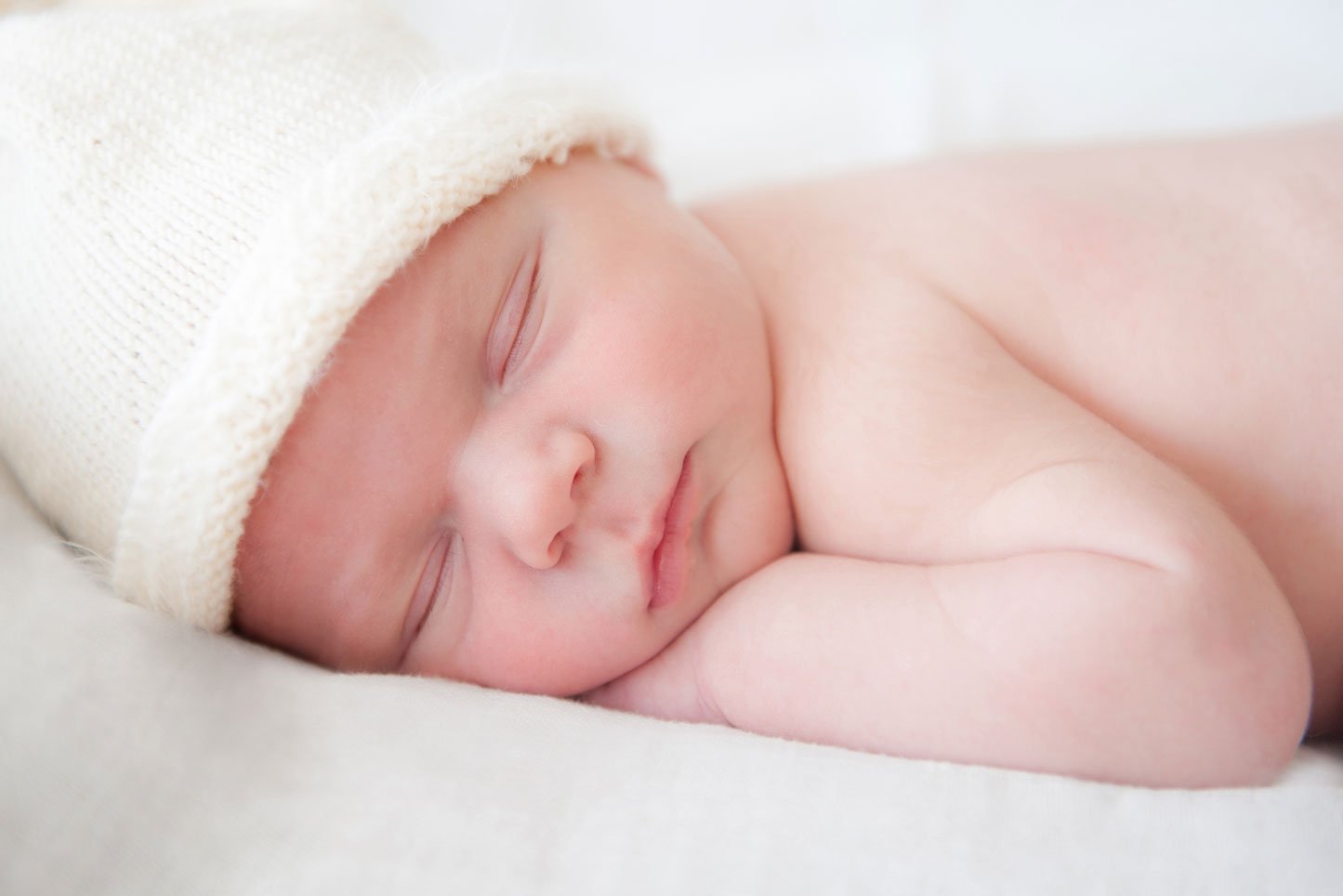 Schlafendes Newborn Baby mit weisser Mütze auf weißem Hintergrund.