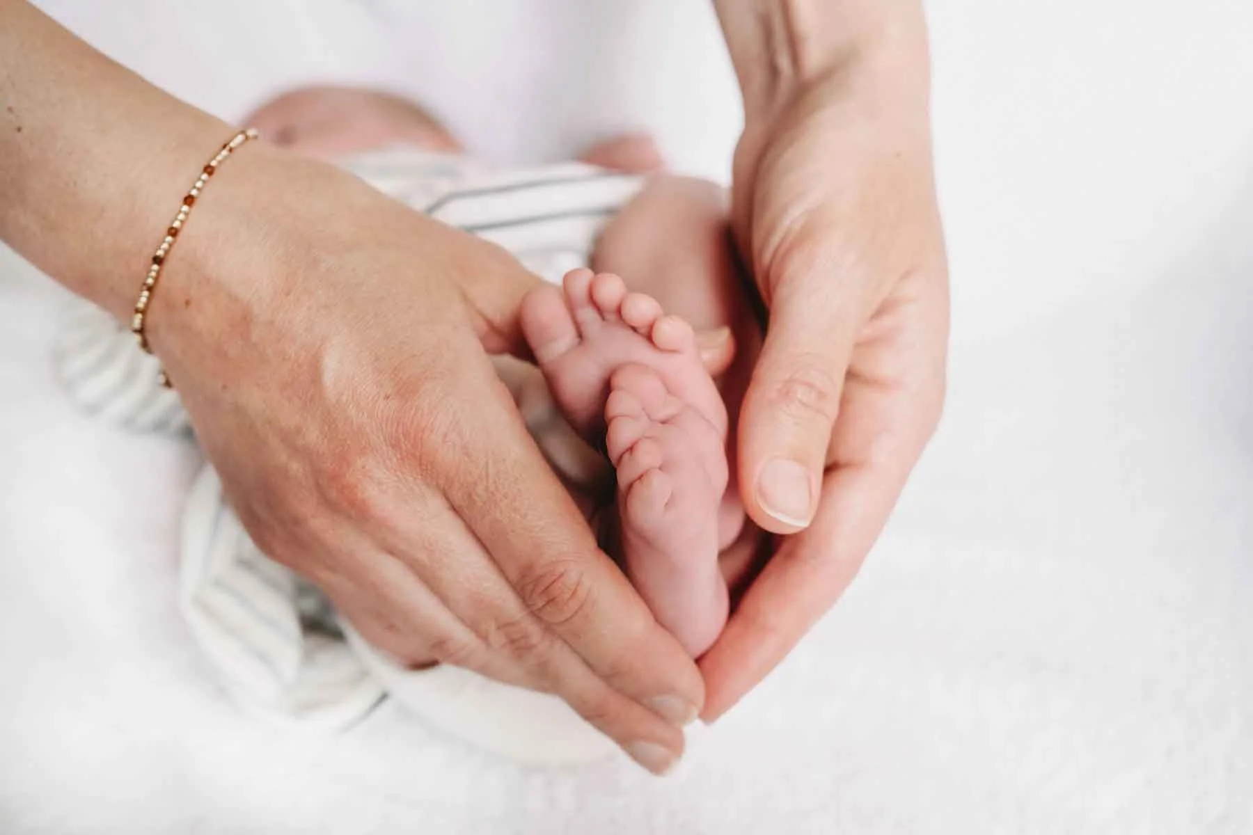 Mama hält die winzigen Füsse ihres Baby, beide Hände bilden ein Herz.