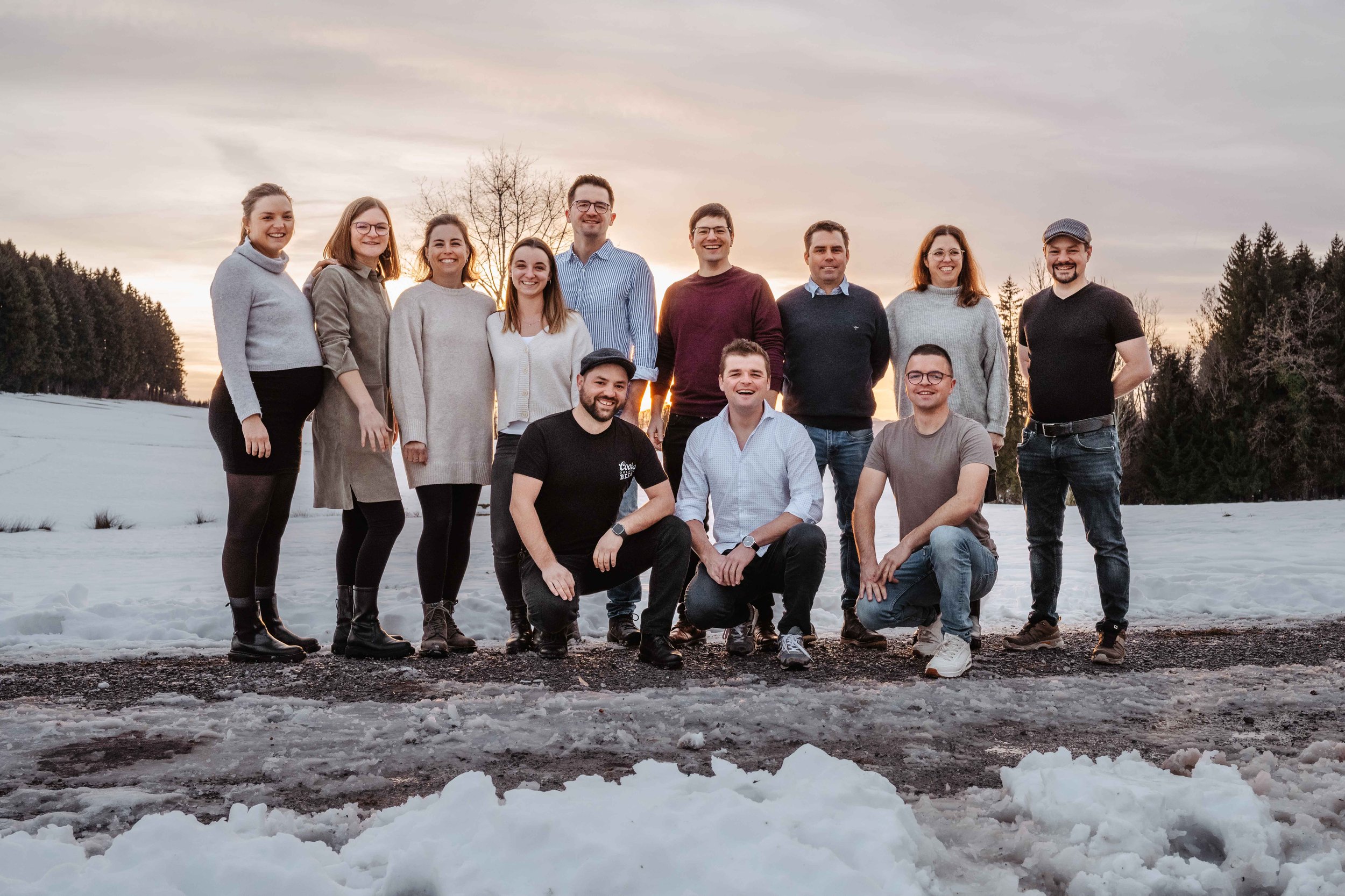 Gruppe von Menschen posiert draussen im Schnee vor einem winterlichen Sonnenuntergang.