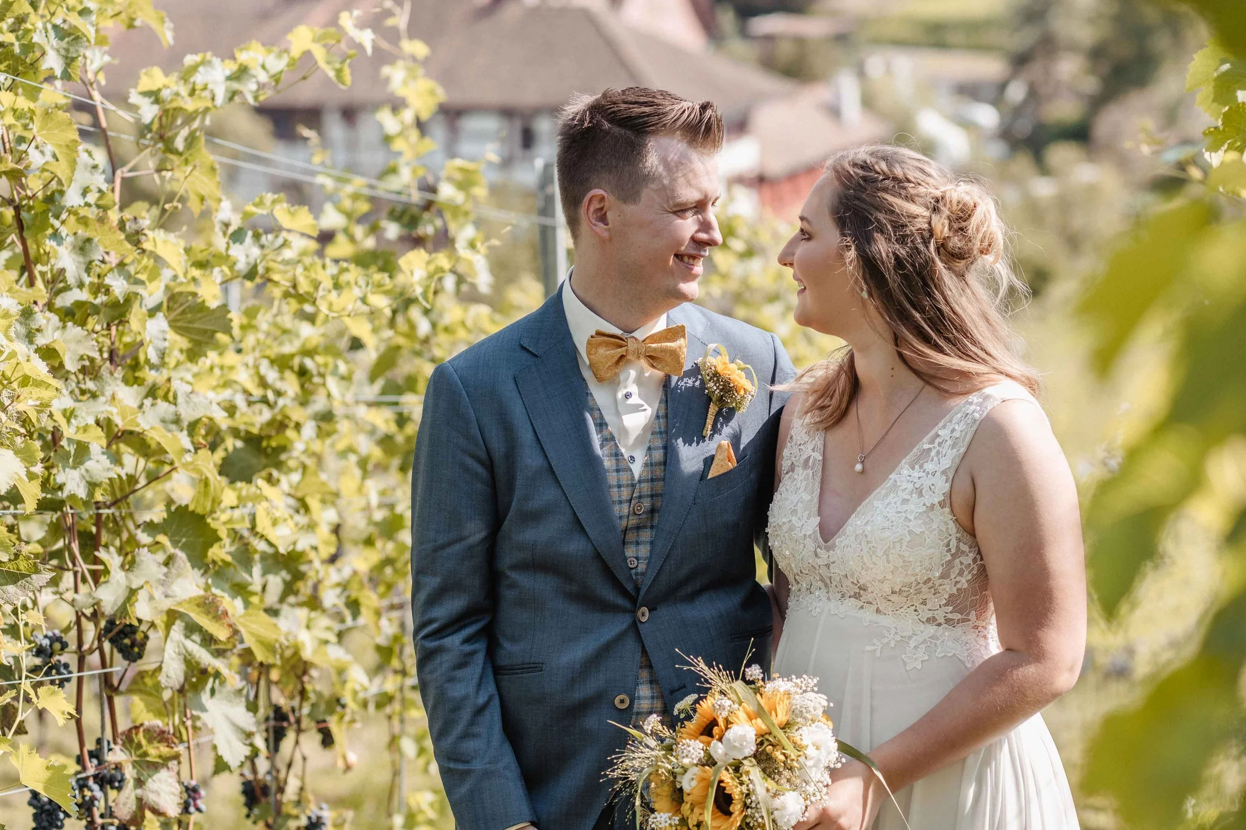 Brautpaar steht in einem Weinberg und blickt sich liebevoll an.