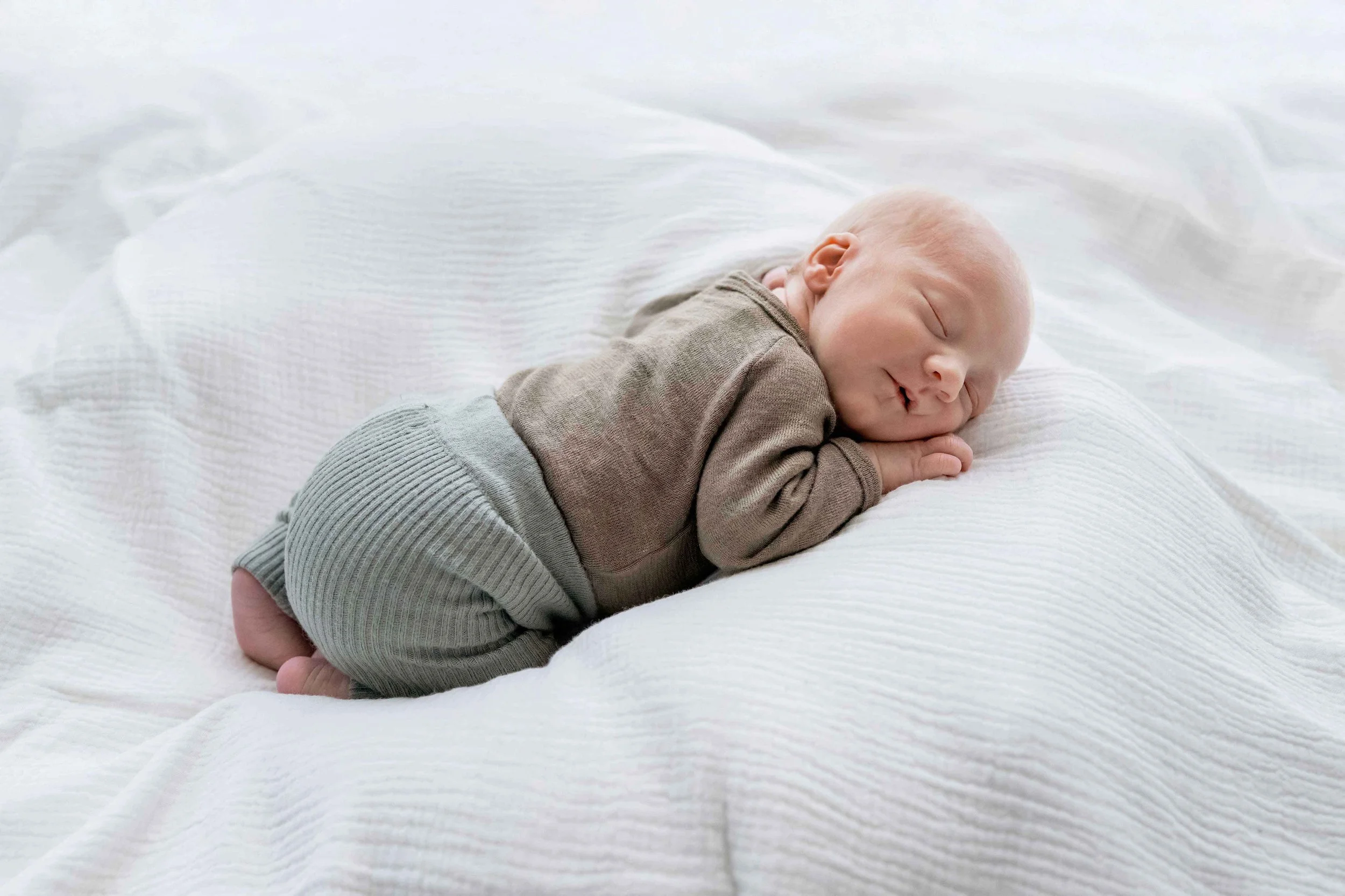 Ein neugeborenes Baby liegt schlafend auf einem weissen Bett.
