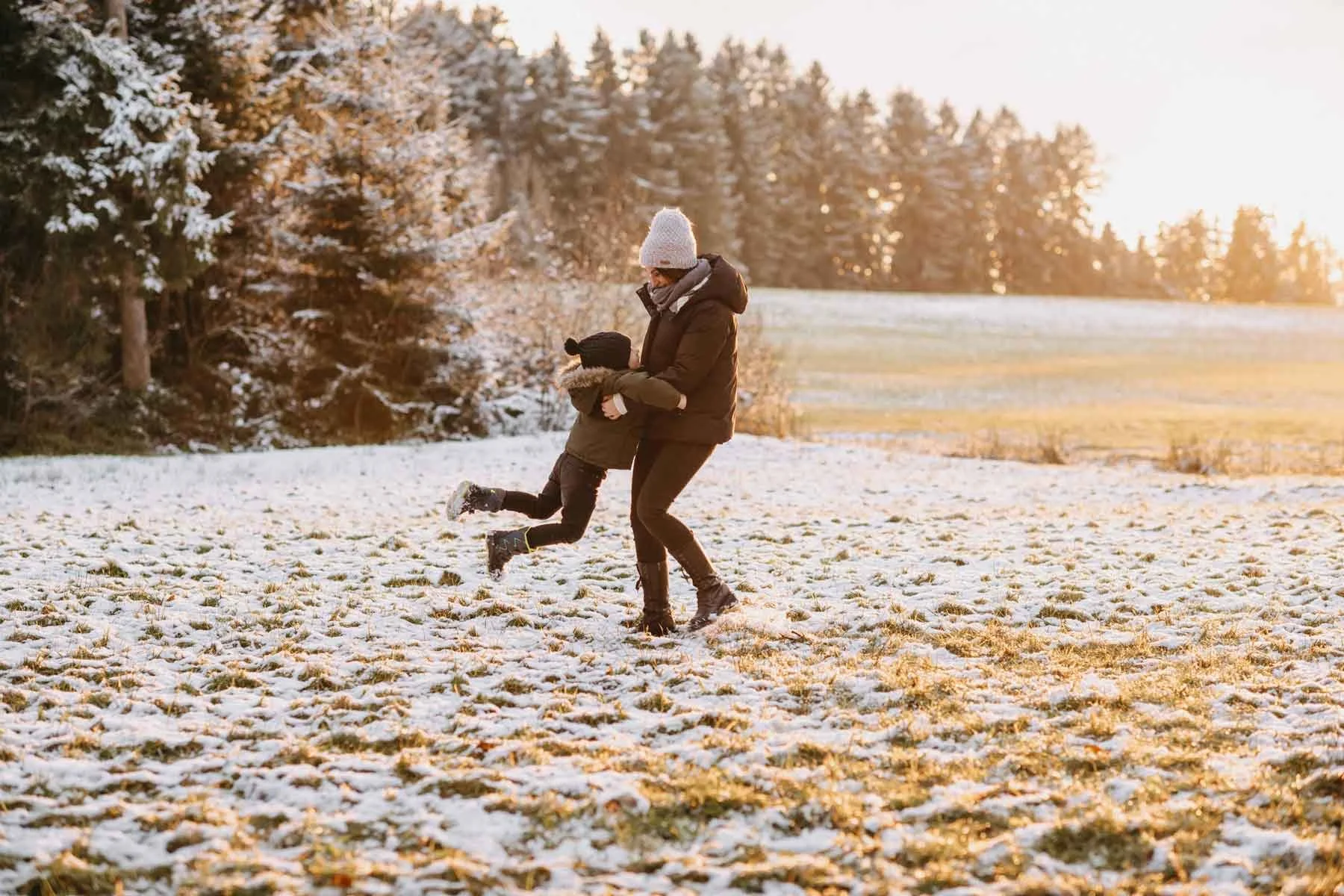 Mutter und Kind in der Natur im Schnee am spielen bei Sonnenuntergang