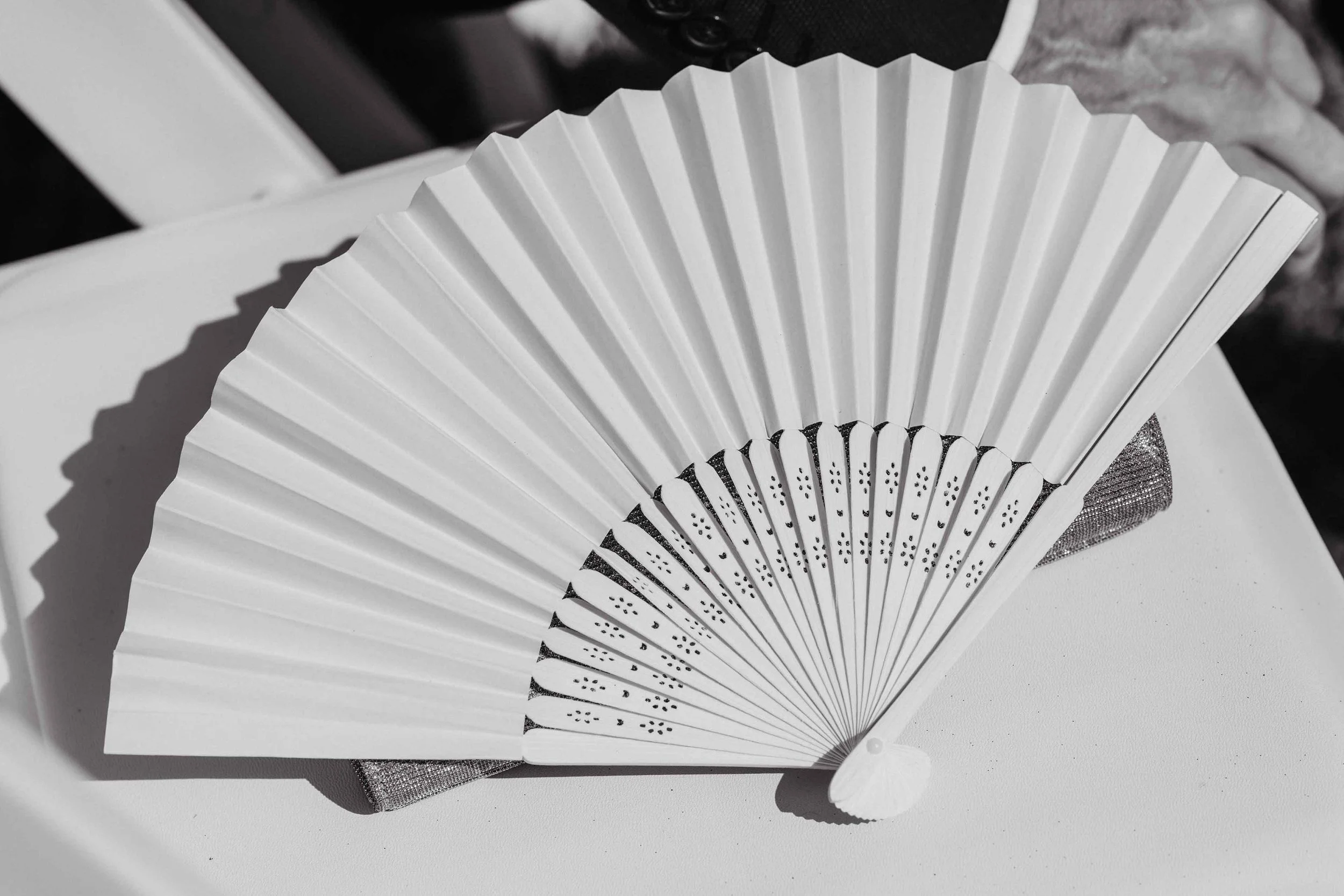 Ein geöffnetes weiße Fächer auf einem Tisch, Schattenwurf sichtbar, Schwarz-Weiss-Fotografie.