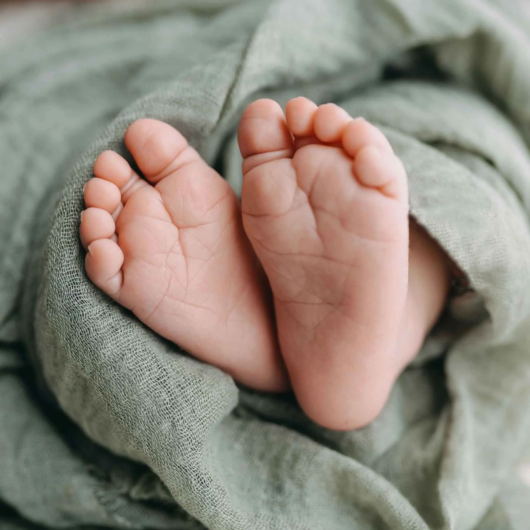 Nahaufnahme von Babyfüssen die eingewickelt in grünem Stoff sind.