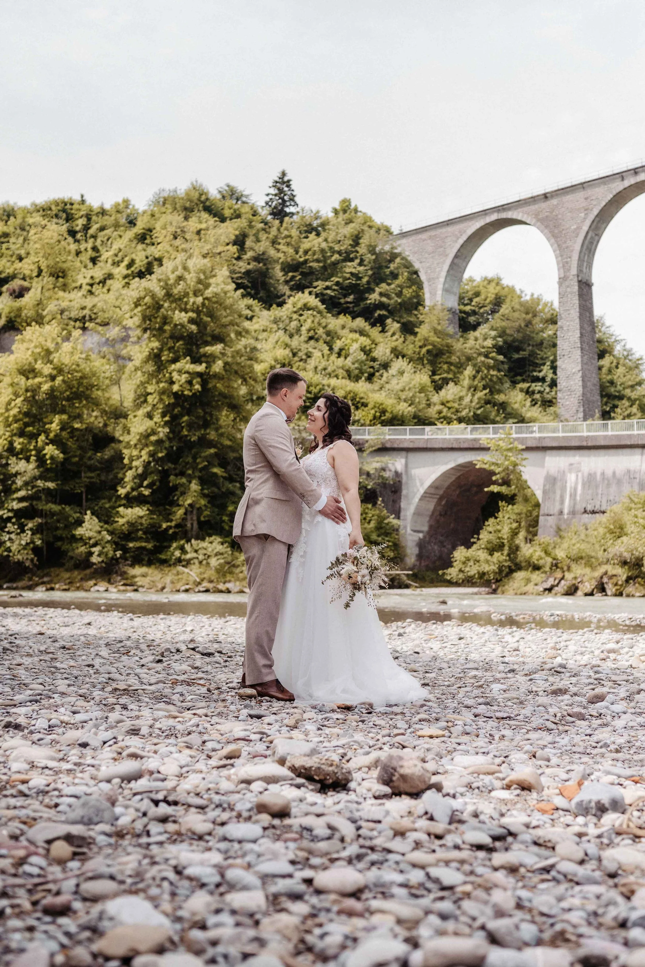 Das Brautpaar steht lächelnd an der Thur, umgeben von grünen Bäumen und dem Viadukt im Hintergrund.