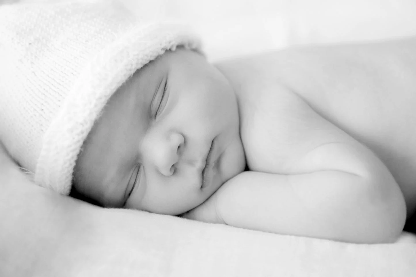 Neugeborenes Baby schläft mit Mütze auf einem weichen Kissen.