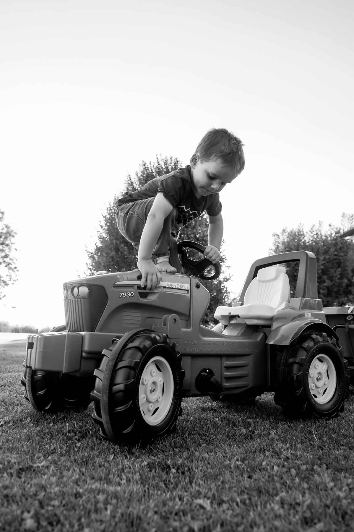 Ein Junge spielt auf einem großen Kindertraktor im Freien, Schwarz-Weiss-Fotografie.