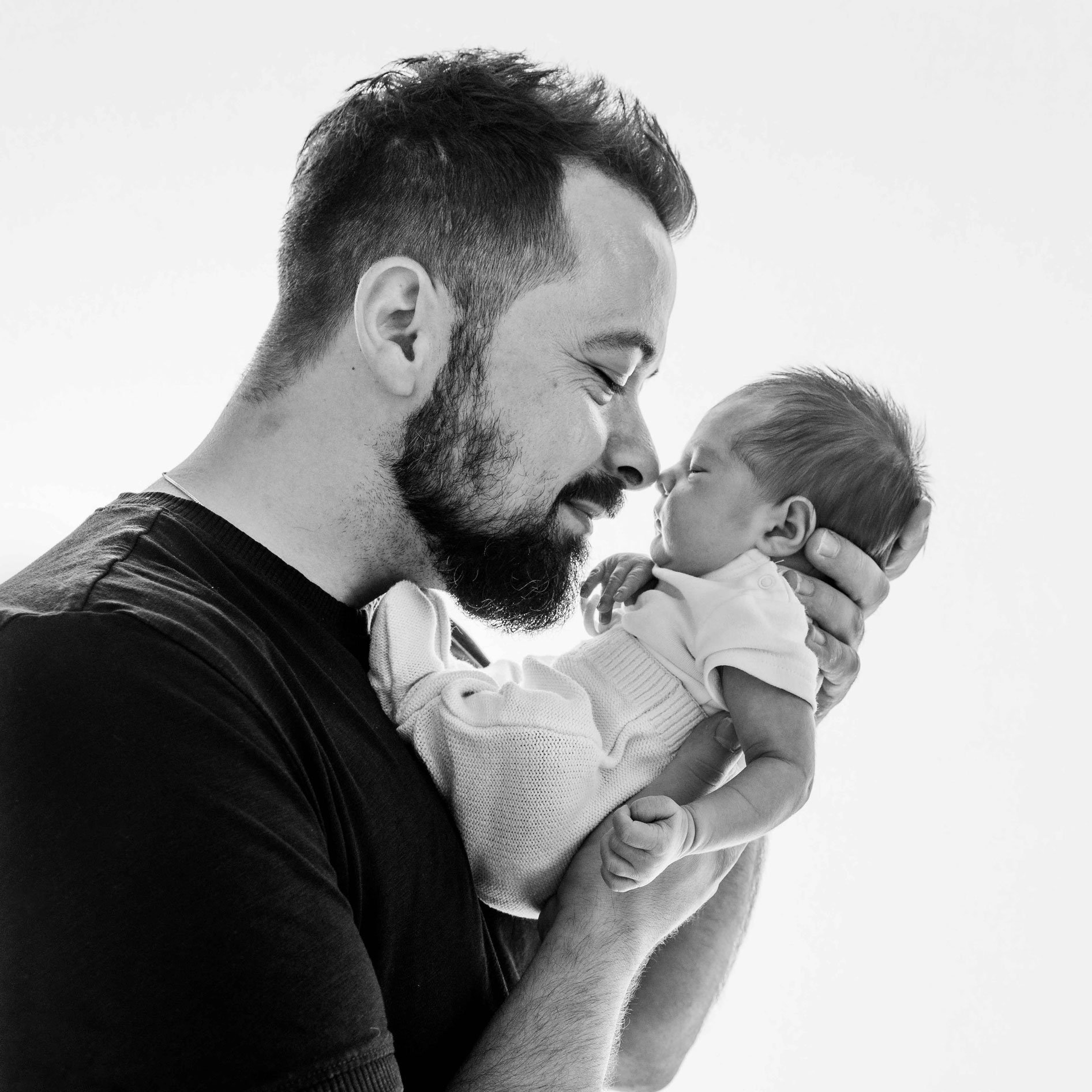 Ein Mann hält sein Baby und beide berühren sanft ihre Nasen. Das Bild ist in Schwarz-Weiss.
