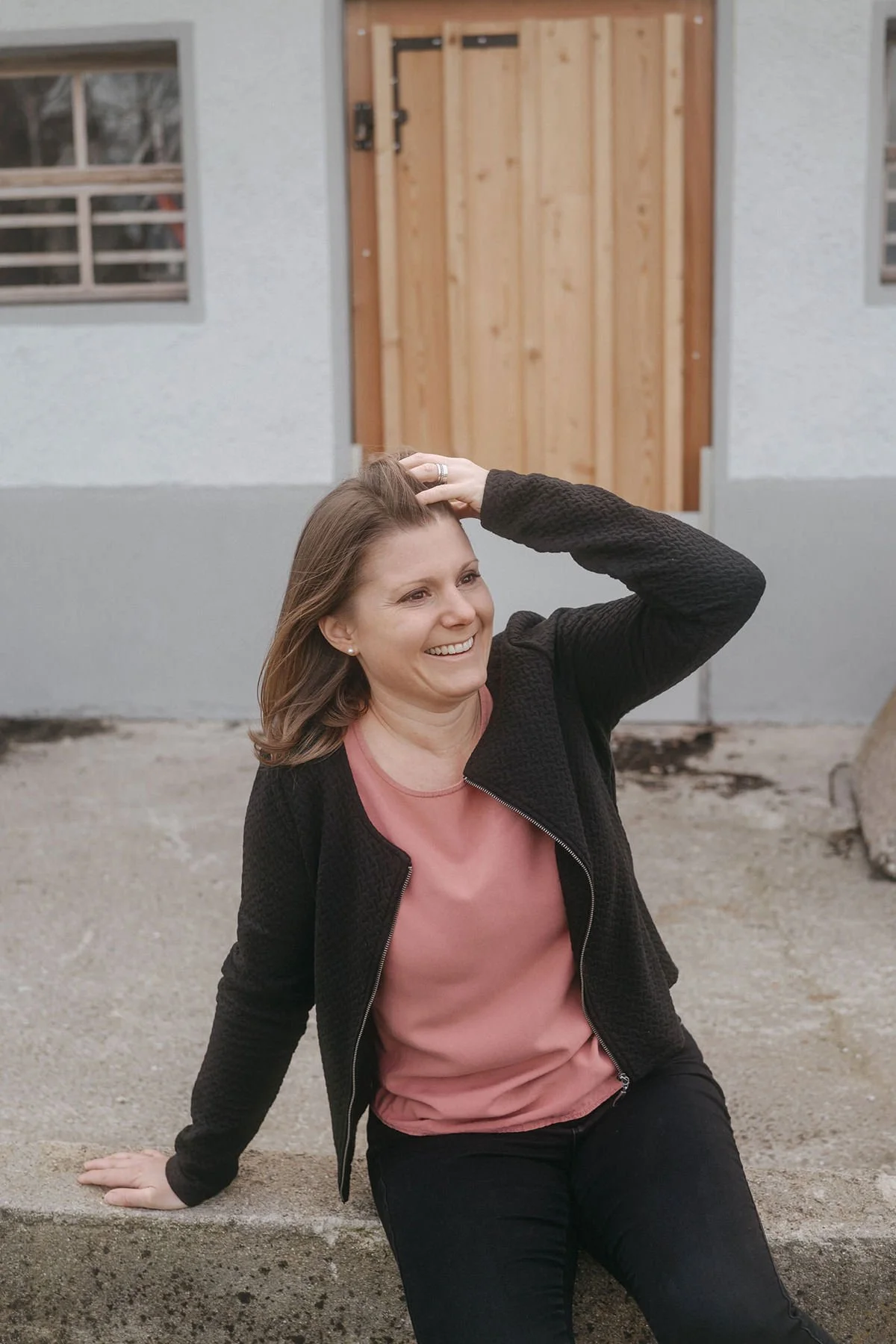 Janine Huber sitzt lachend auf einem Betonblock vor einem Gebäude