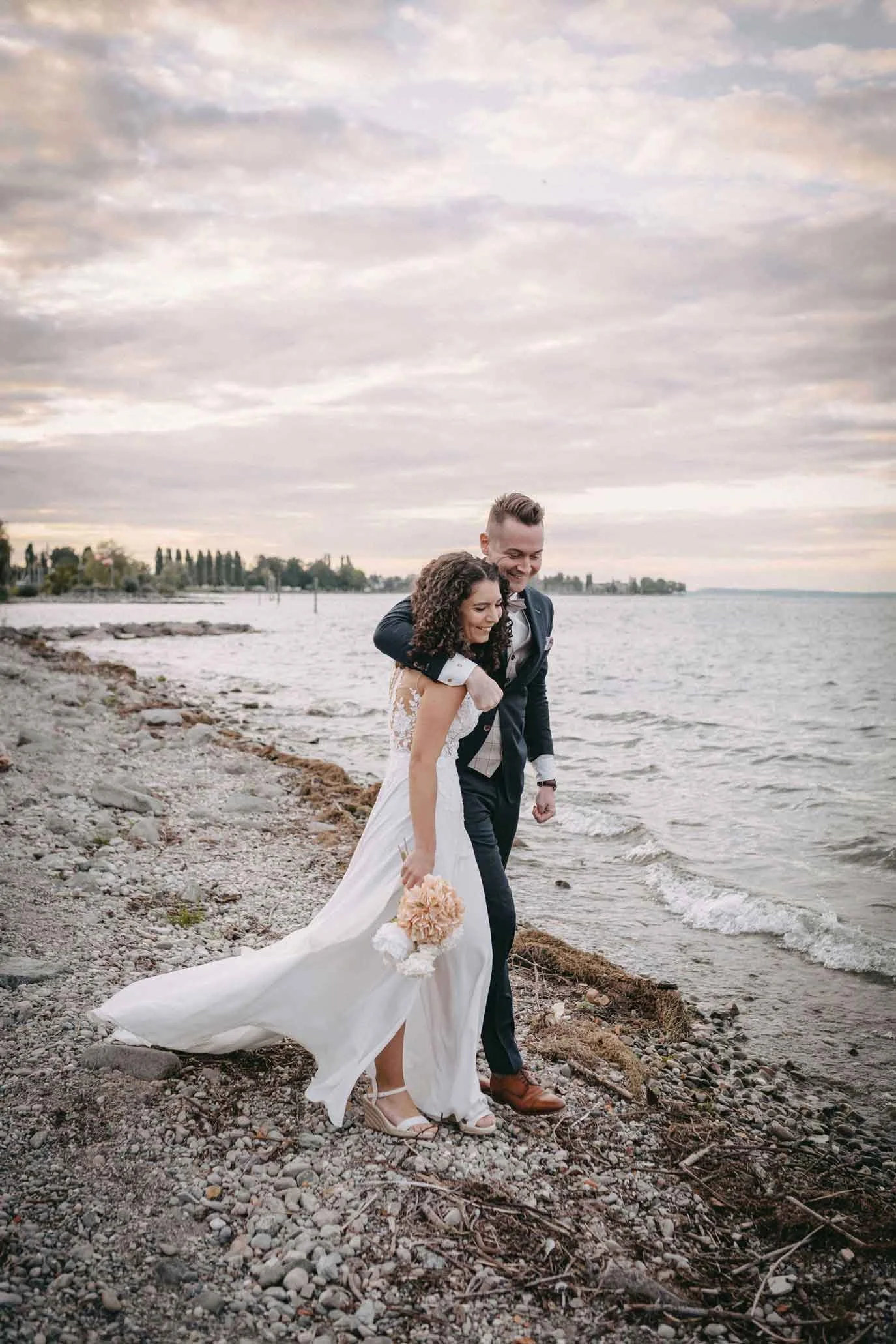 Hochzeitspaar am Strand bei Sonnenuntergang, das sich gegenseitig umarmt.