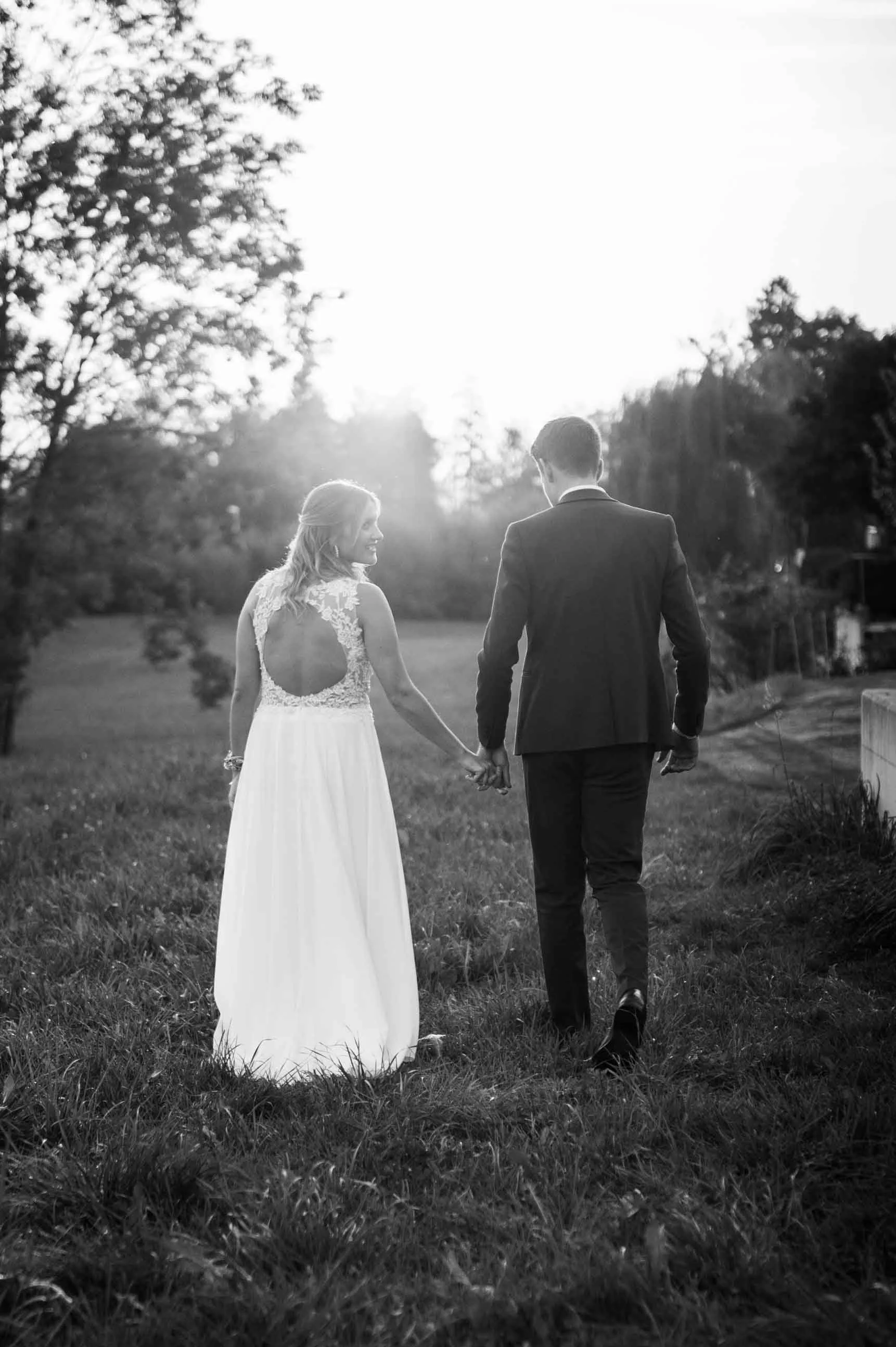 Brautpaar hält Händchen beim Spaziergang im Freien bei Sonnenuntergang, schwarz-weiss Foto.