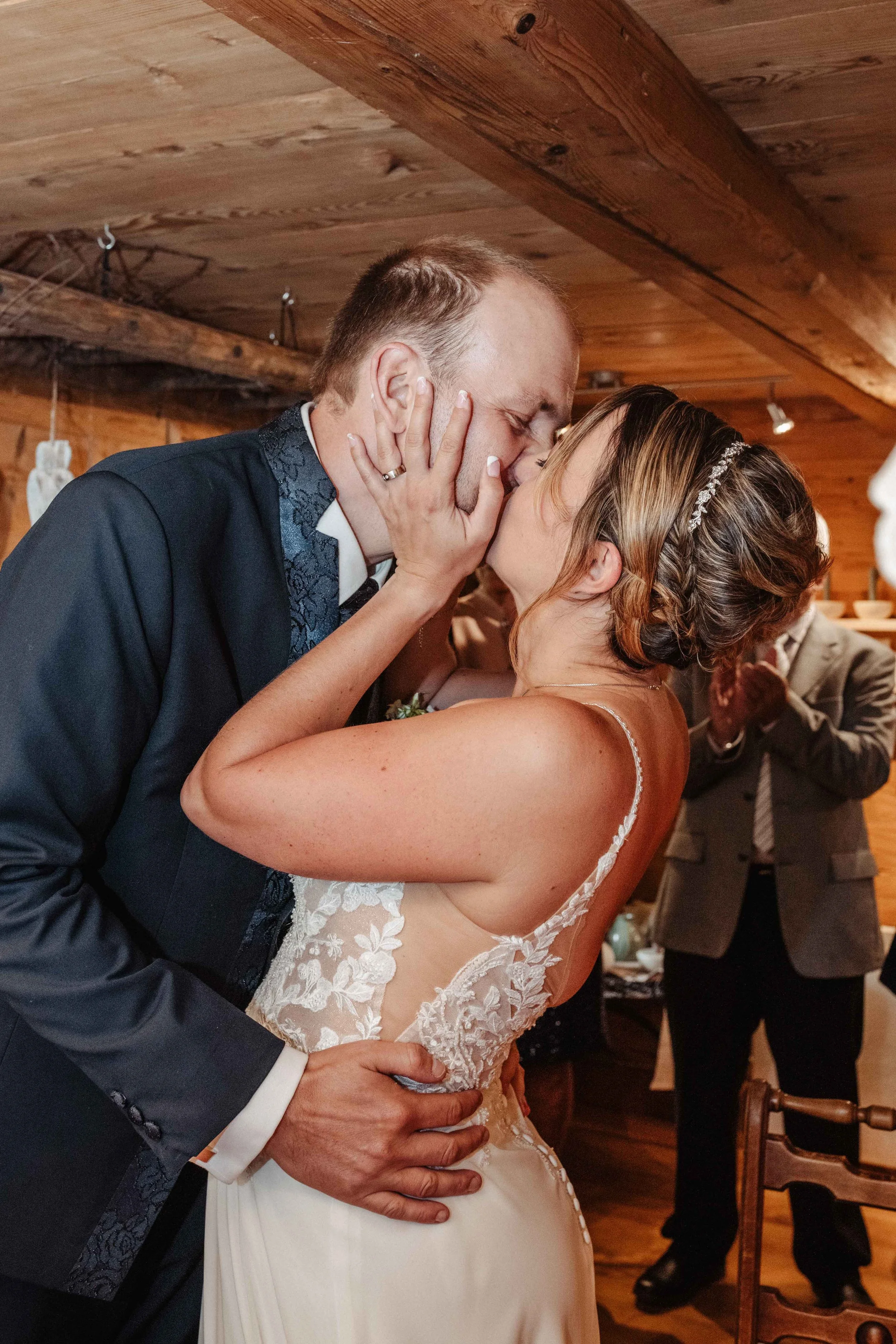 Hochzeitspaar küsst sich in einer romantischen Umarmung bei ihrer Hochzeit in einem rustikalen Holzraum.