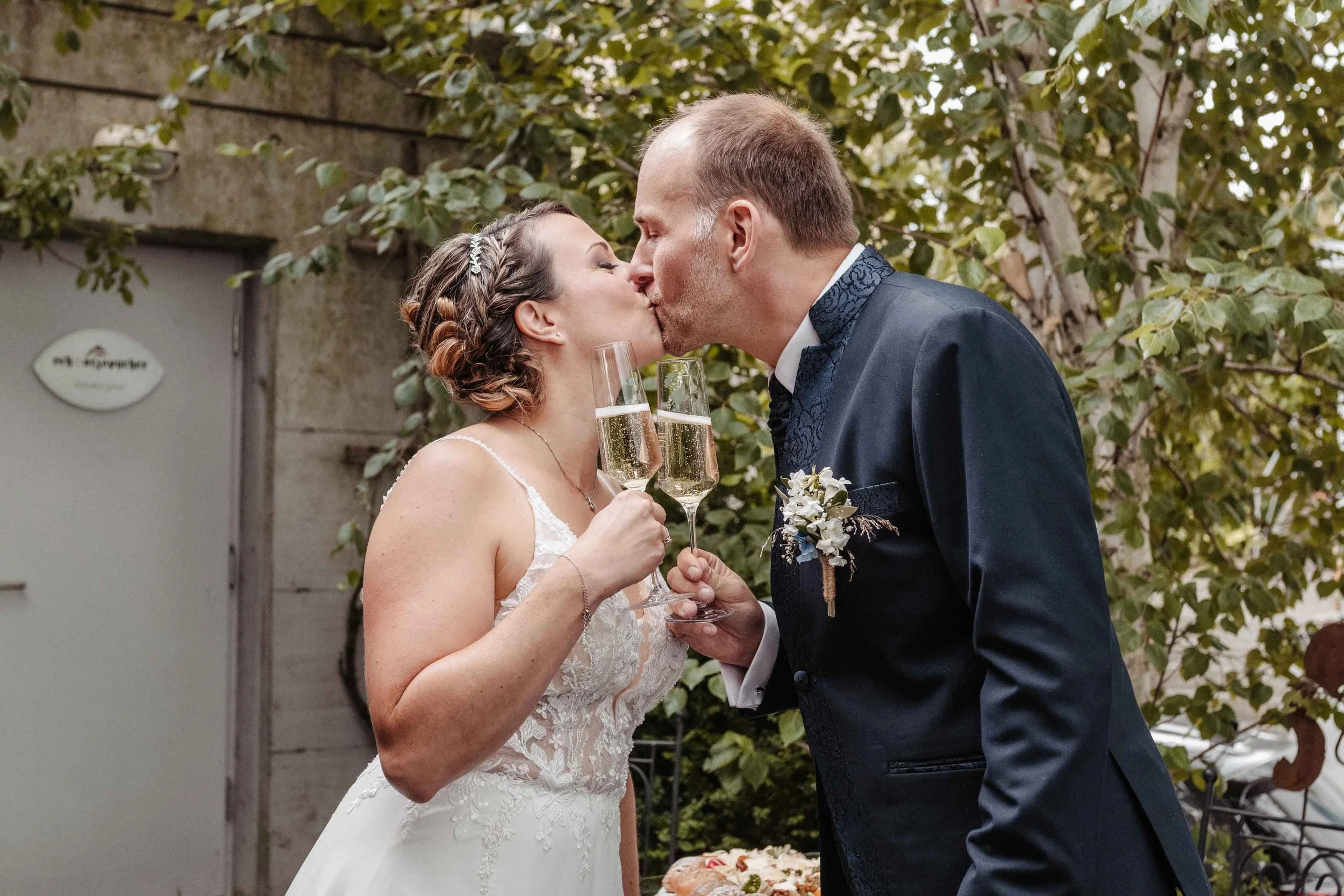 Brautpaar bei der Hochzeitsfeier, das sich küsst und Champagner trinkt.