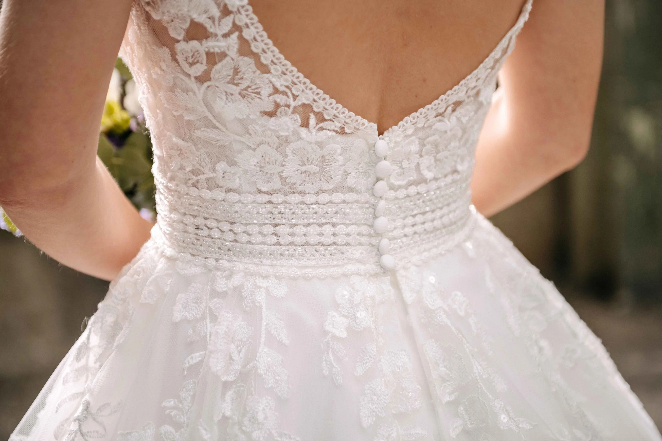 Nahaufnahme eines weissen Hochzeitskleids mit Spitzenmuster und Perlendetails