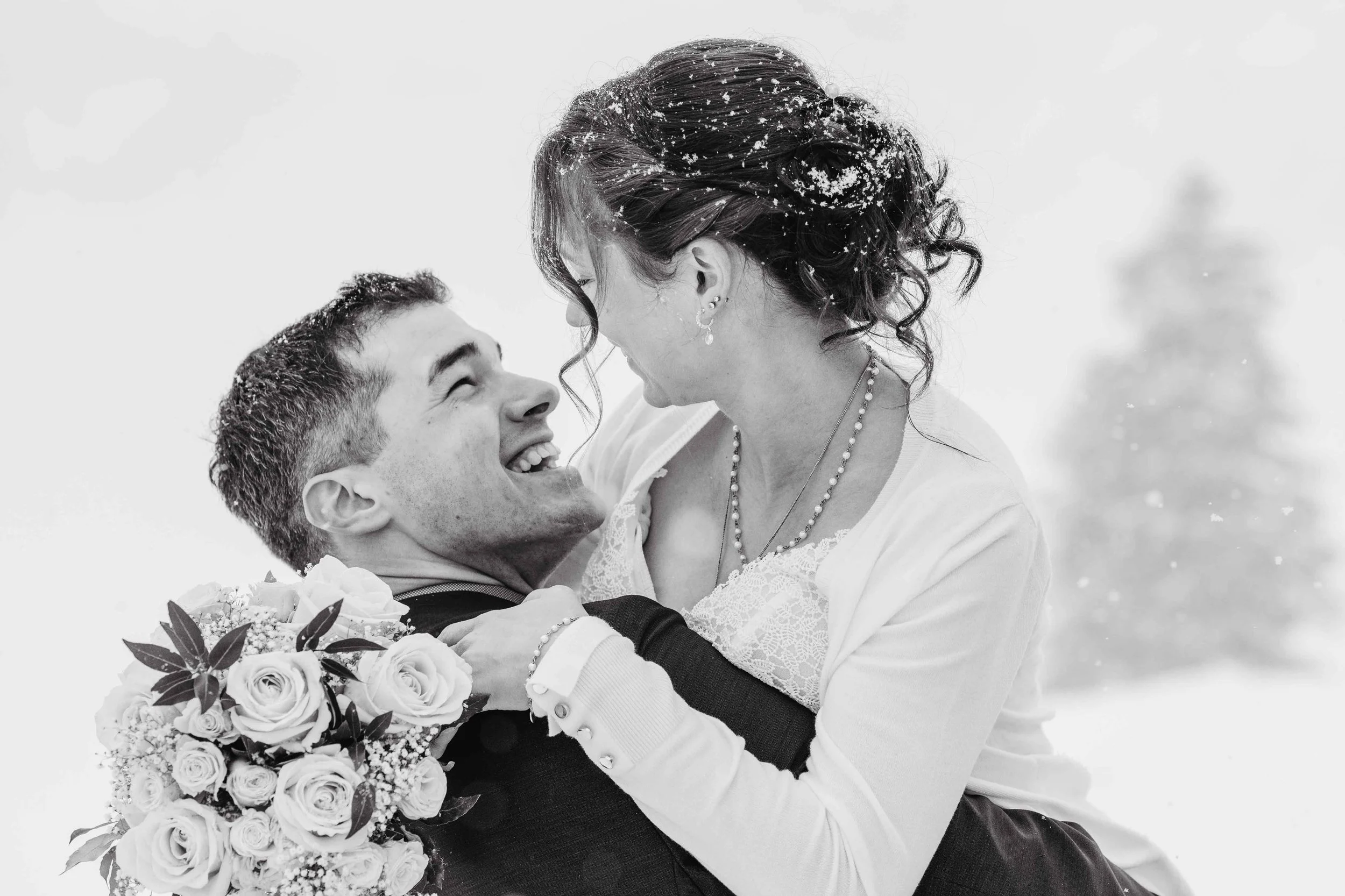 Ein glückliches Hochzeitspaar im Schnee, der Braut hält den Bräutigam in den Armen, sie lachen zusammen.