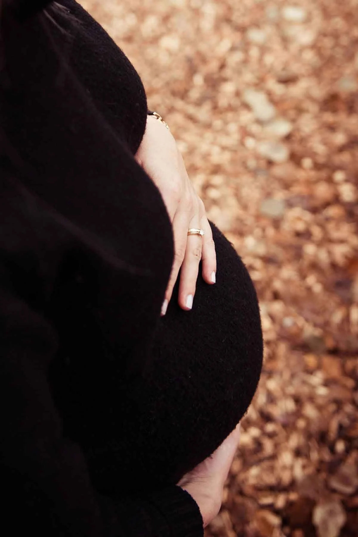Nahaufnahme einer schwangeren Frau, die ihren Bauch mit einer Hand hält.