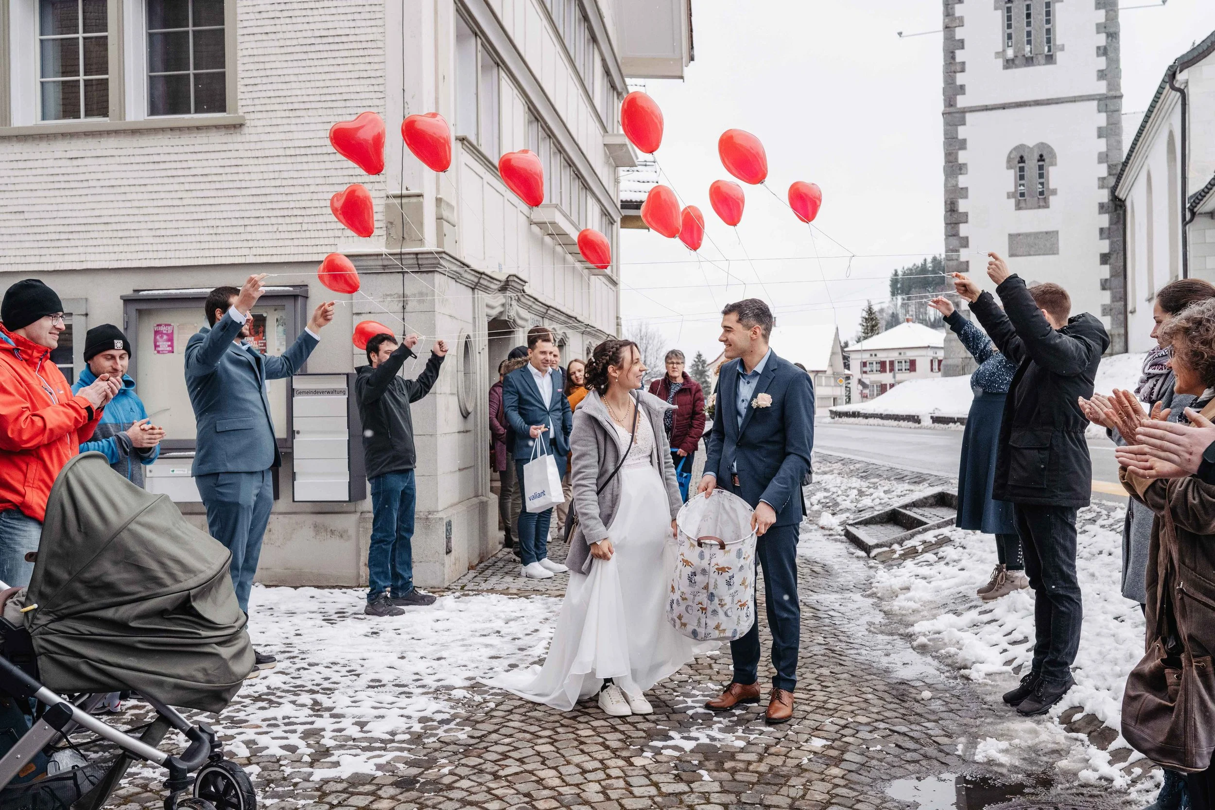 Ein frisch verheiratetes Paar werden von Freunden und Familie mit roten Herzballons empfangen.