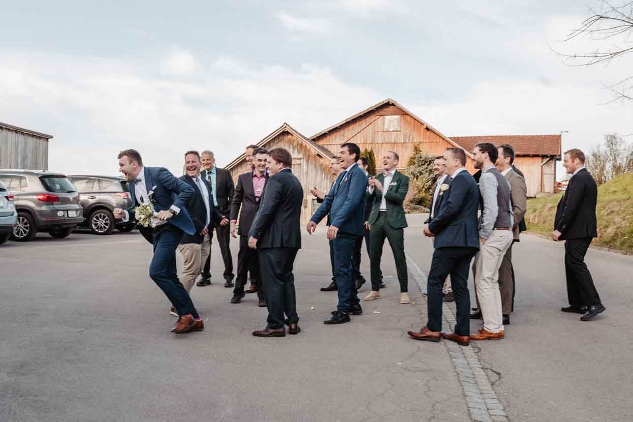 Männer in Anzügen, die lachen und ein Mann mit dem Brautstrauss.