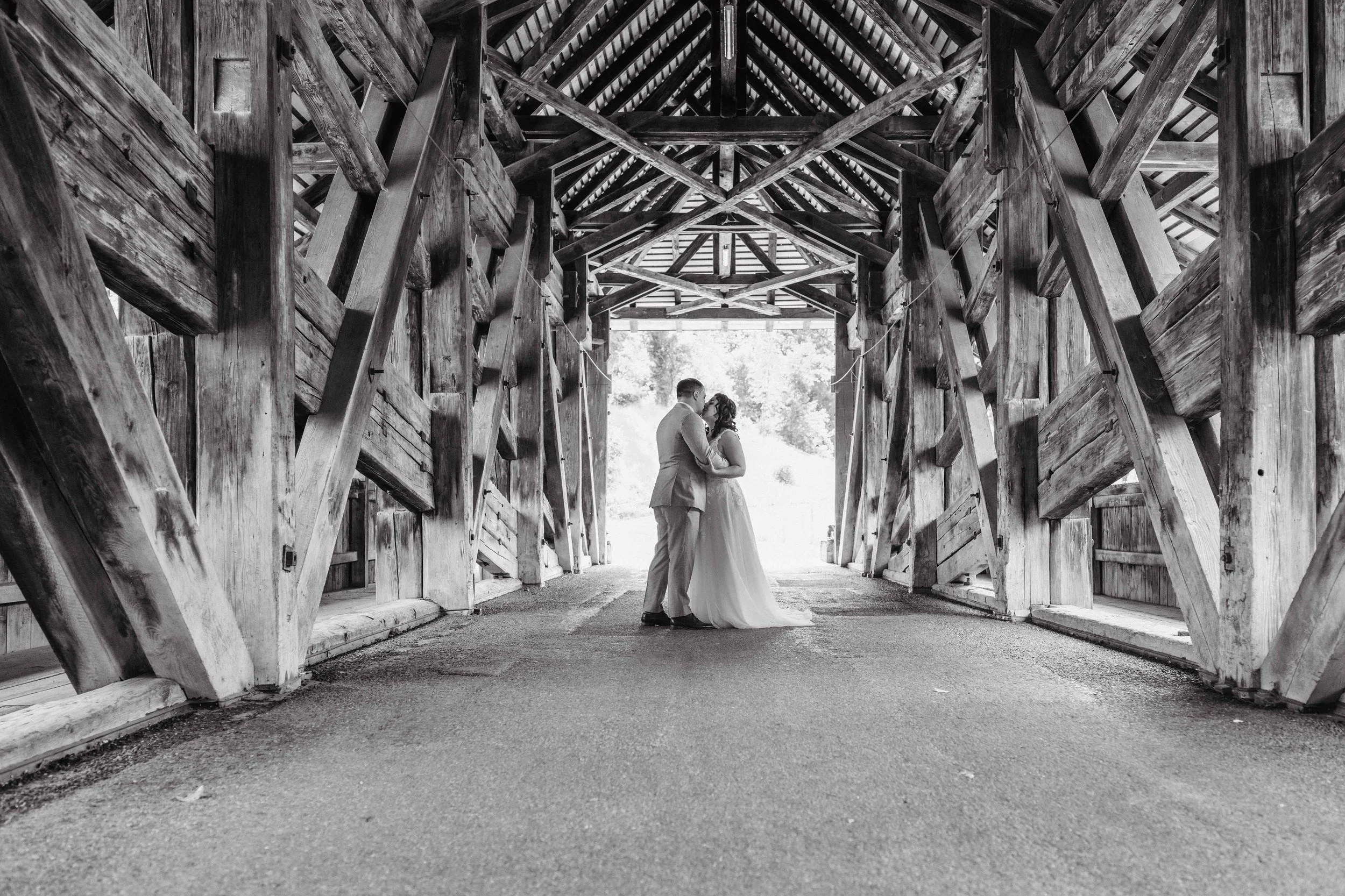 Braut und Bräutigam einer alten Holzbrücke, Blick auf deren Umarmung, schwarz-weiß Fotografie.