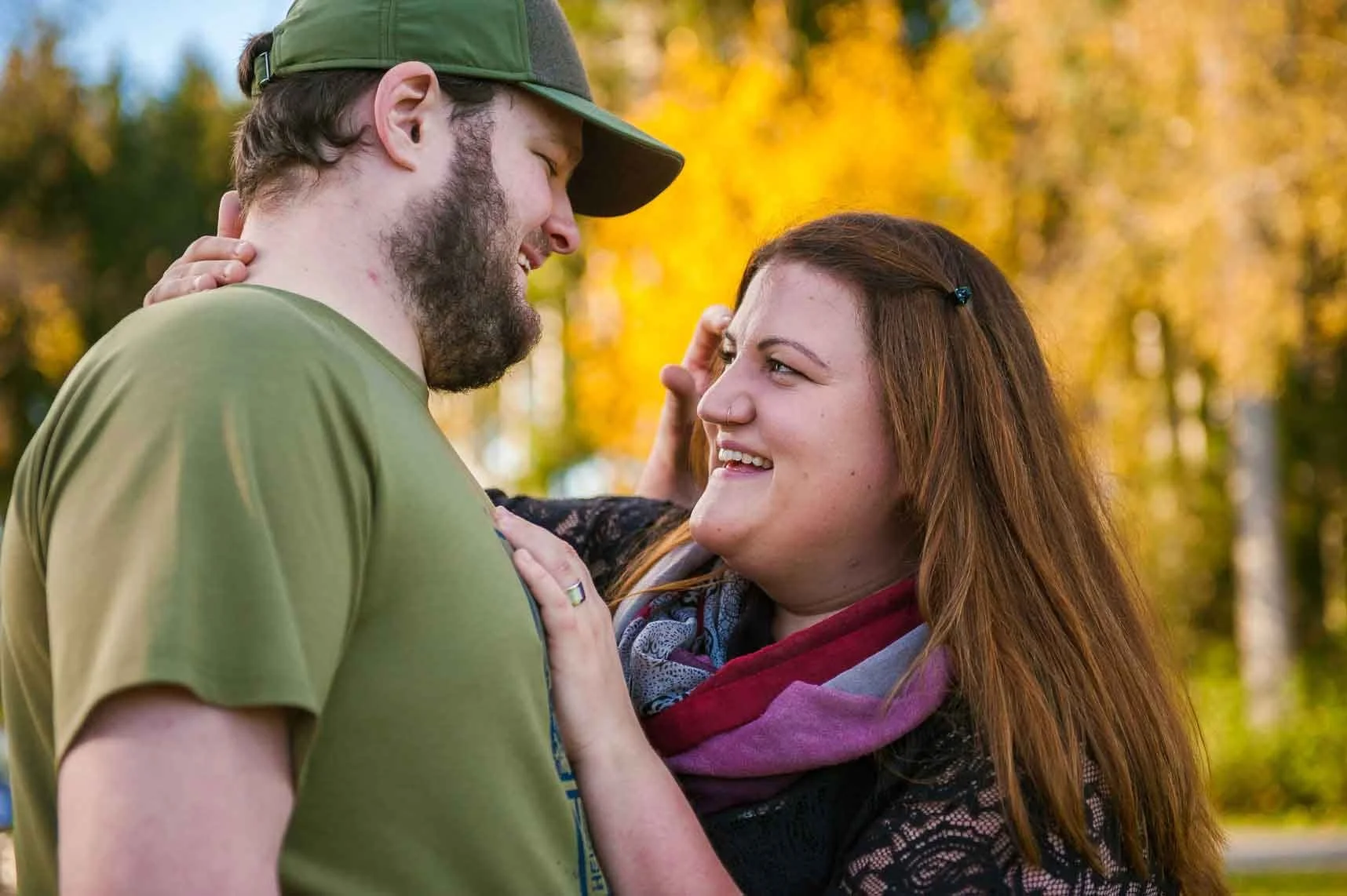 Ein lachendes Paar steht sich nahe im Park an einem sonnigen Herbsttag, umgeben von goldgelben Blättern, und schaut sich liebevoll in die Augen.