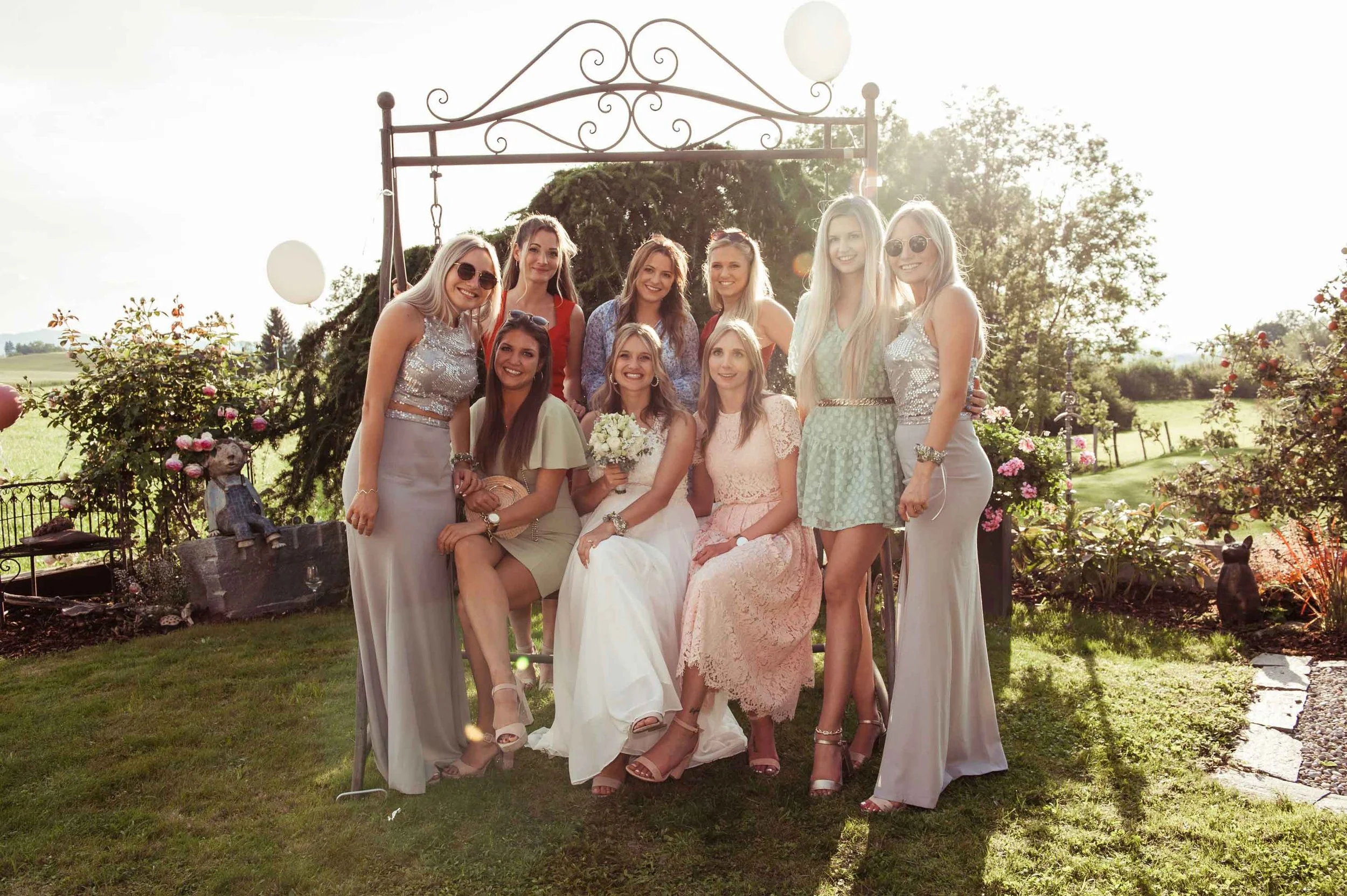 Gruppe von Frauen bei einer Hochzeitsfeier mit der Braut in der Mitte und Sonnenlicht im Hintergrund.