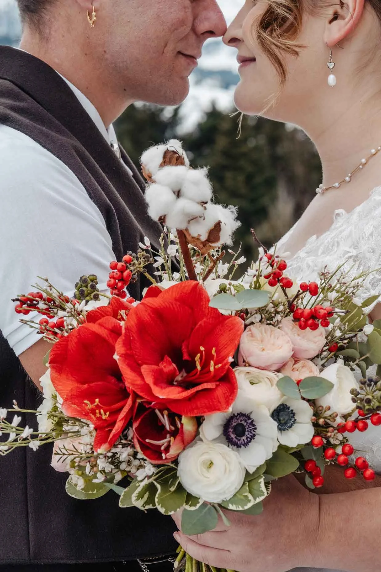 Paar, das sich bei einer Hochzeit fast berührt, im Vordergrund Brautstrauss mit roten Amaryllis, weißen Anemonen, Rosen, Beeren und Eukalyptus.