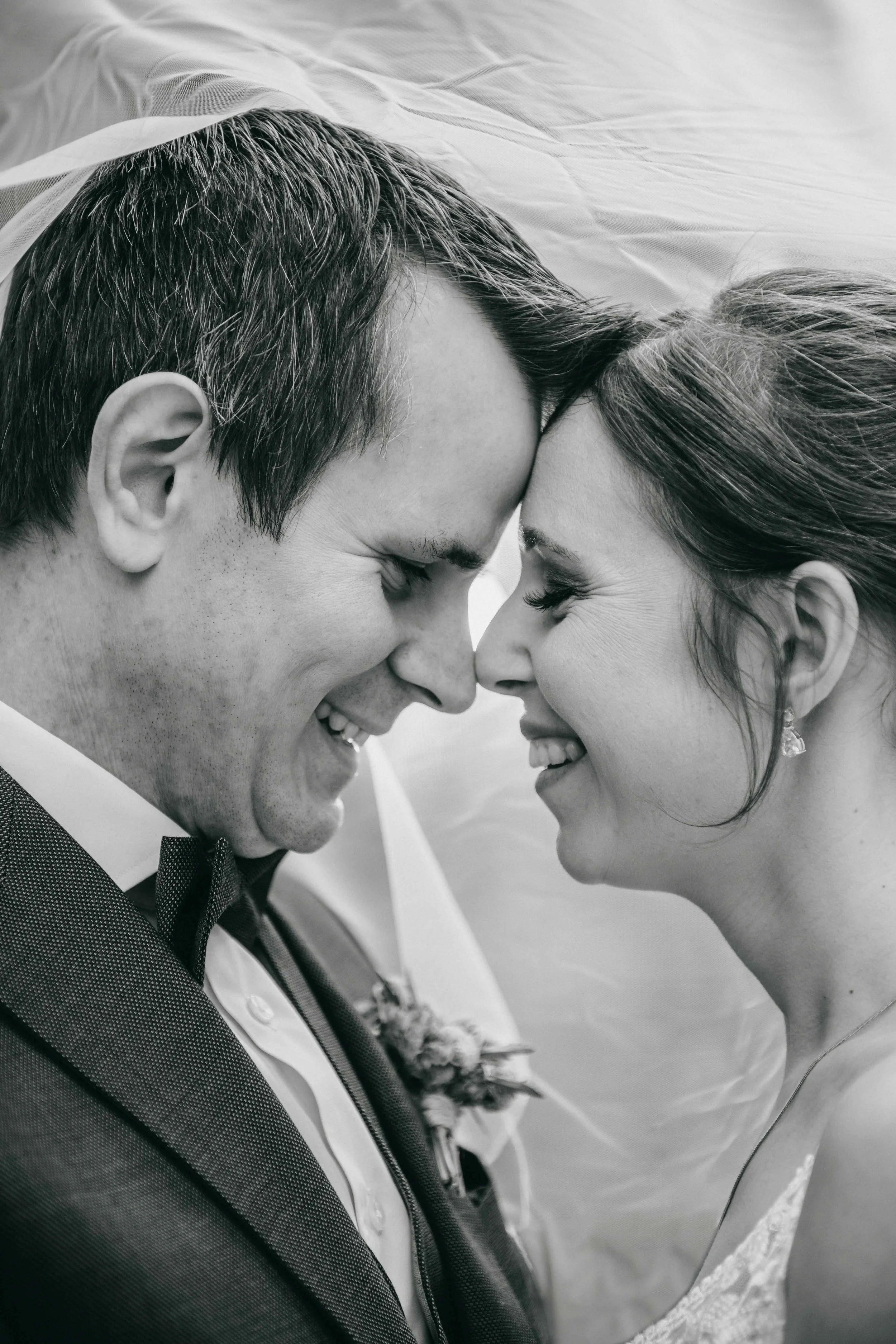 Ein glückliches Brautpaar auf einer Hochzeit, lächelnd eng beieinander, mit Stirn an Stirn, schwarz-weiss aufgenommen.