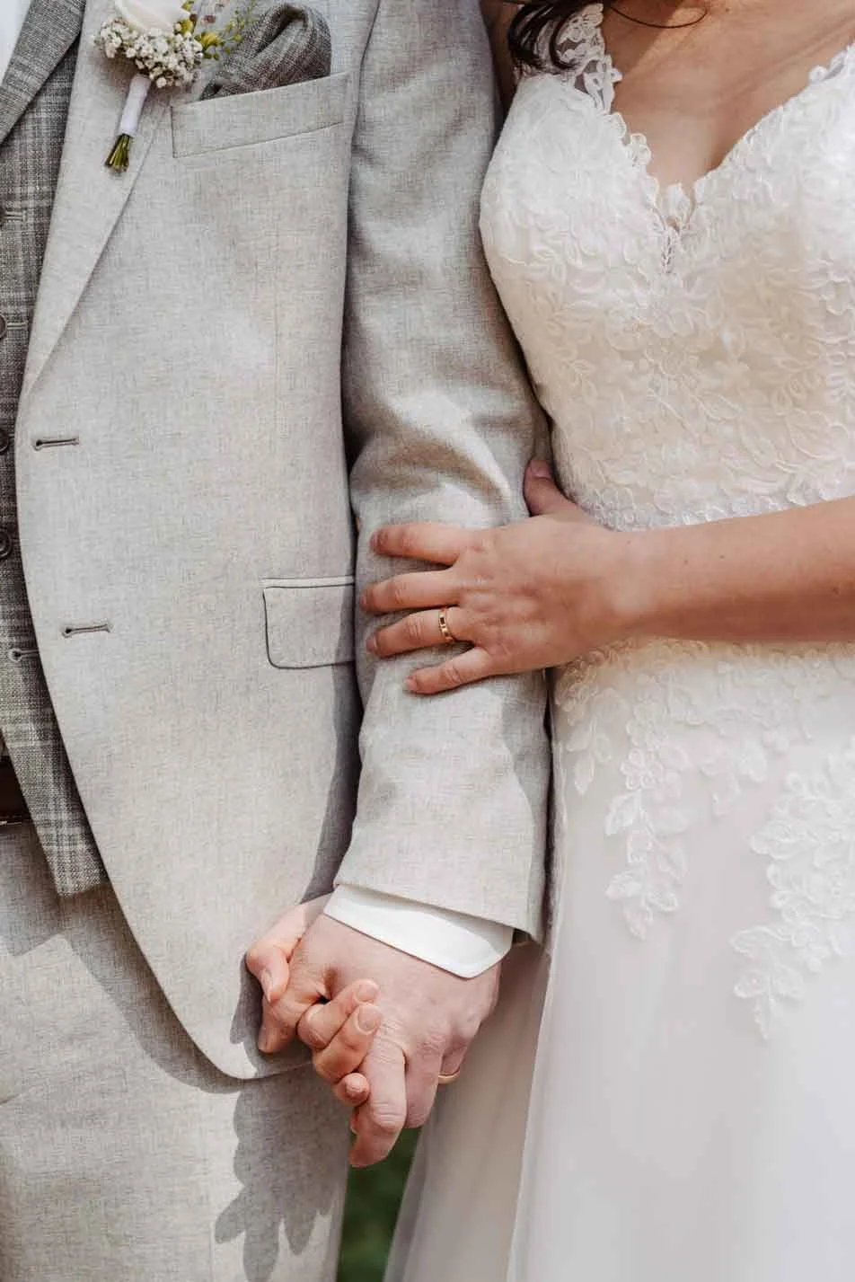 Nahaufnahme eines Brautpaares, das sich an den Händen hält, mit Ehering sichtbar.