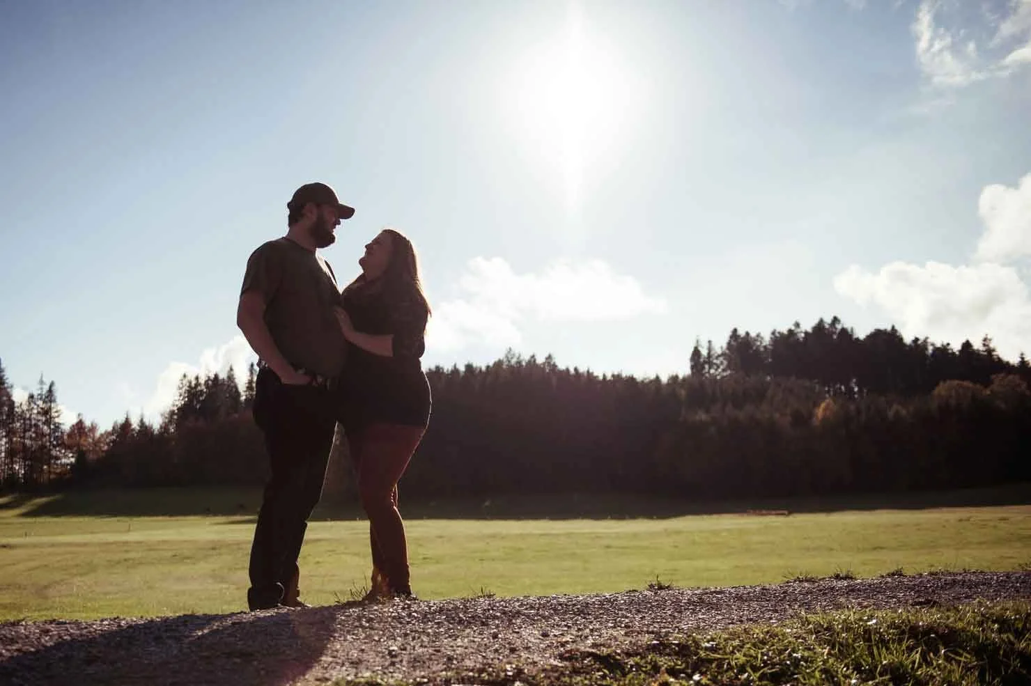 Ein Paar steht sich bei Sonnenuntergang oder Sonnenaufgang auf einer Wiese gegenüber, umgeben von Bäumen.